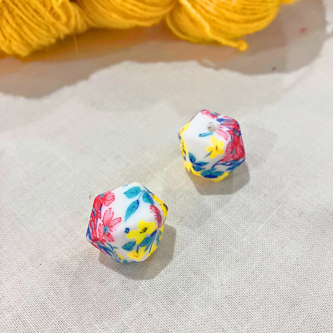 Colourful, geometric stitch stoppers on a lightly textured surface with yellow yarn in the background