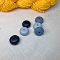Monochrome, geometric stitch stoppers on a lightly textured surface with yellow yarn in the background