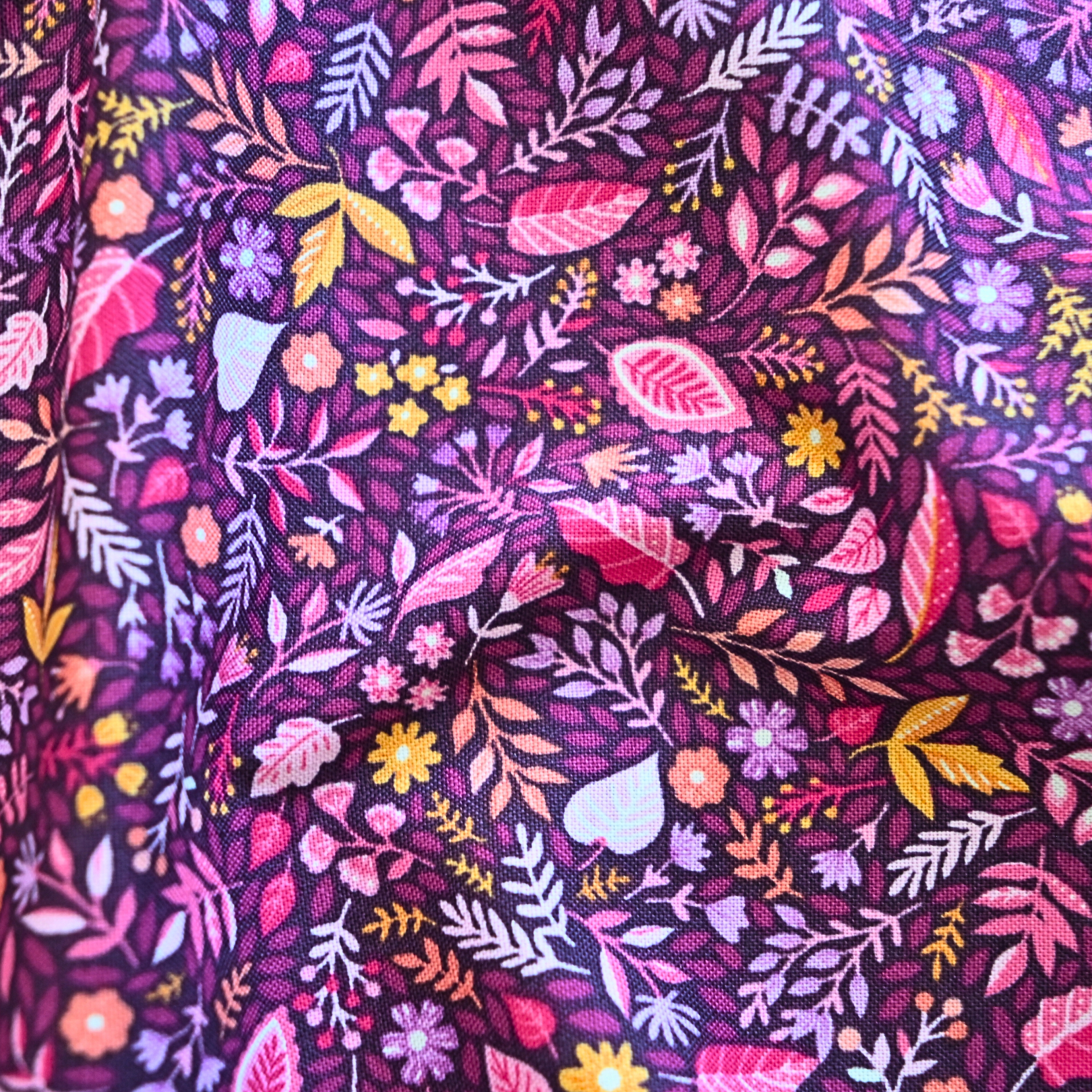 Close-up of floral fabric pattern with pink, purple, and yellow colors on a dark background.