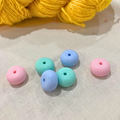 Pastel-coloured, oval stitch stoppers on a lightly textured surface with yellow yarn in the background