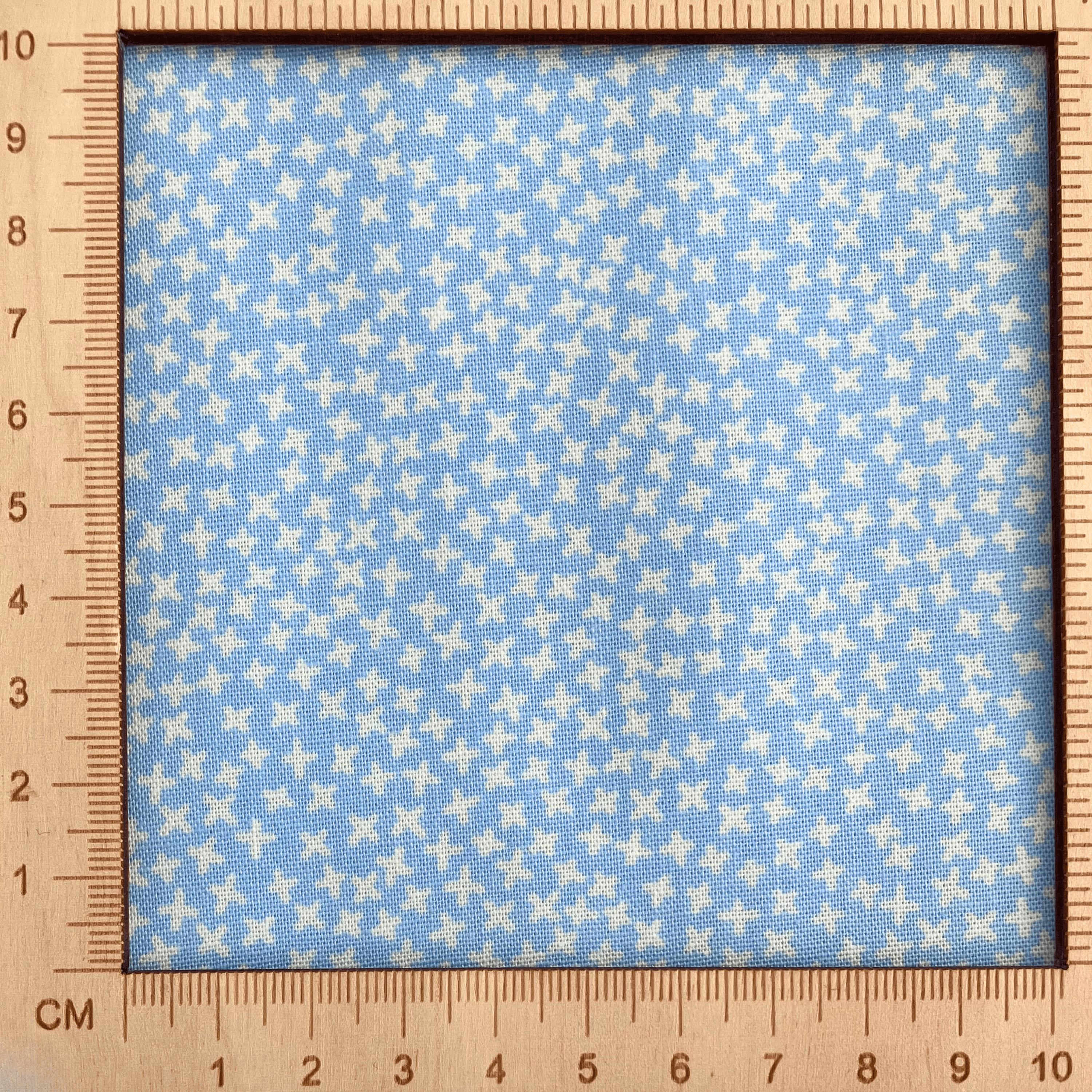 Fabric with small white cross pattern on a blue background, measured by a wooden ruler.