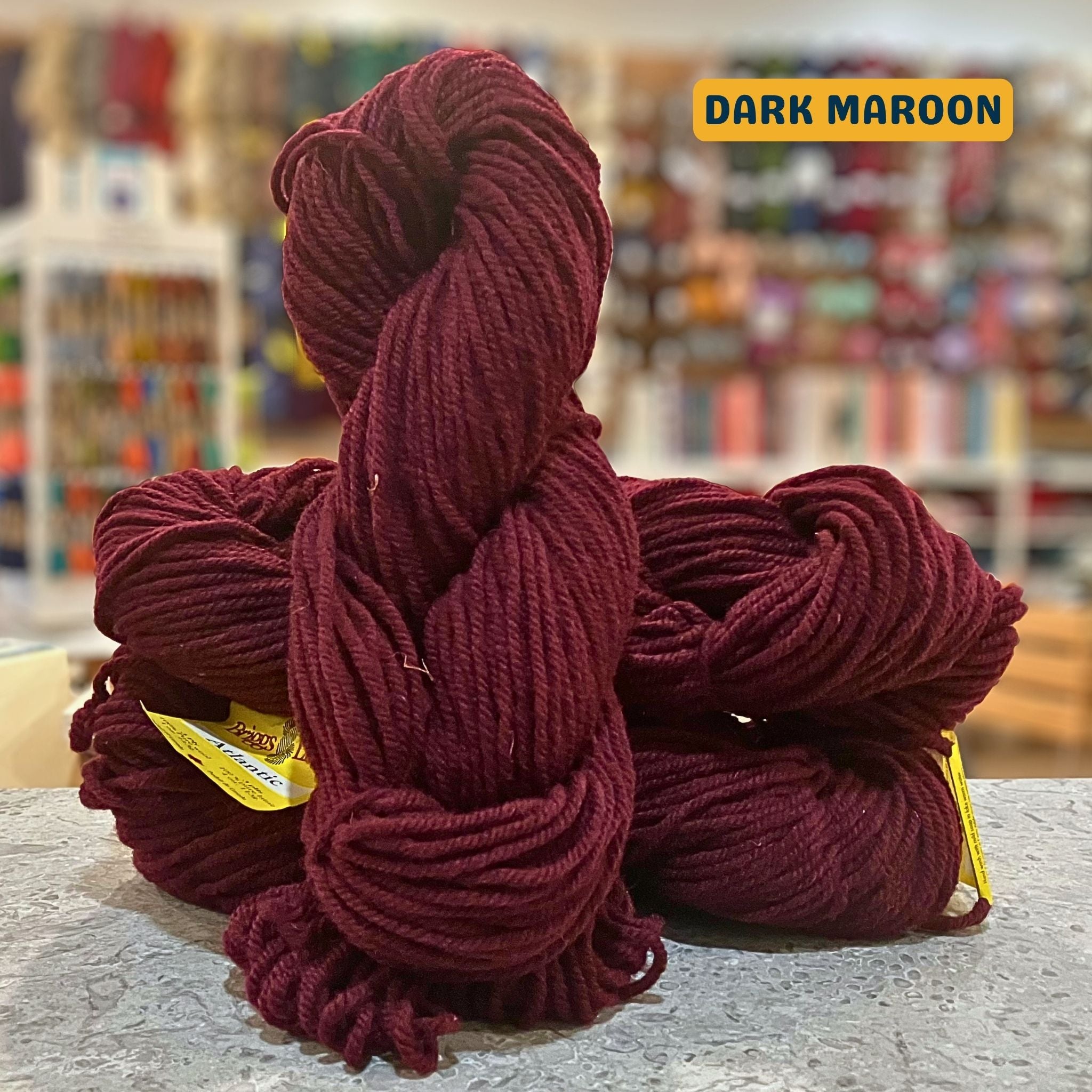 113g wine red (dark maroon) Canadian wool bulky skein, Briggs & Little yarn, craft shop background (blurred)
