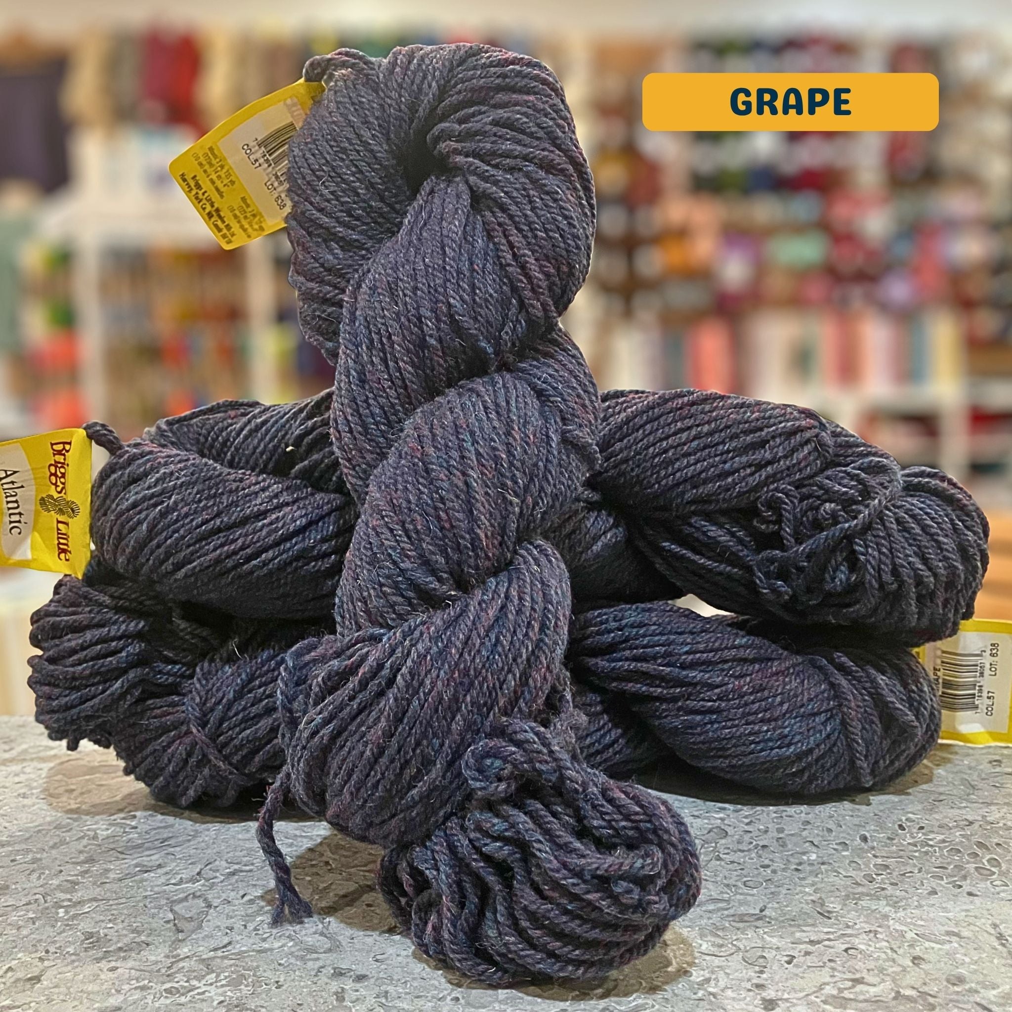 113g heathered grey-purple (grape) Canadian wool bulky skein, Briggs & Little yarn, craft shop background (blurred)