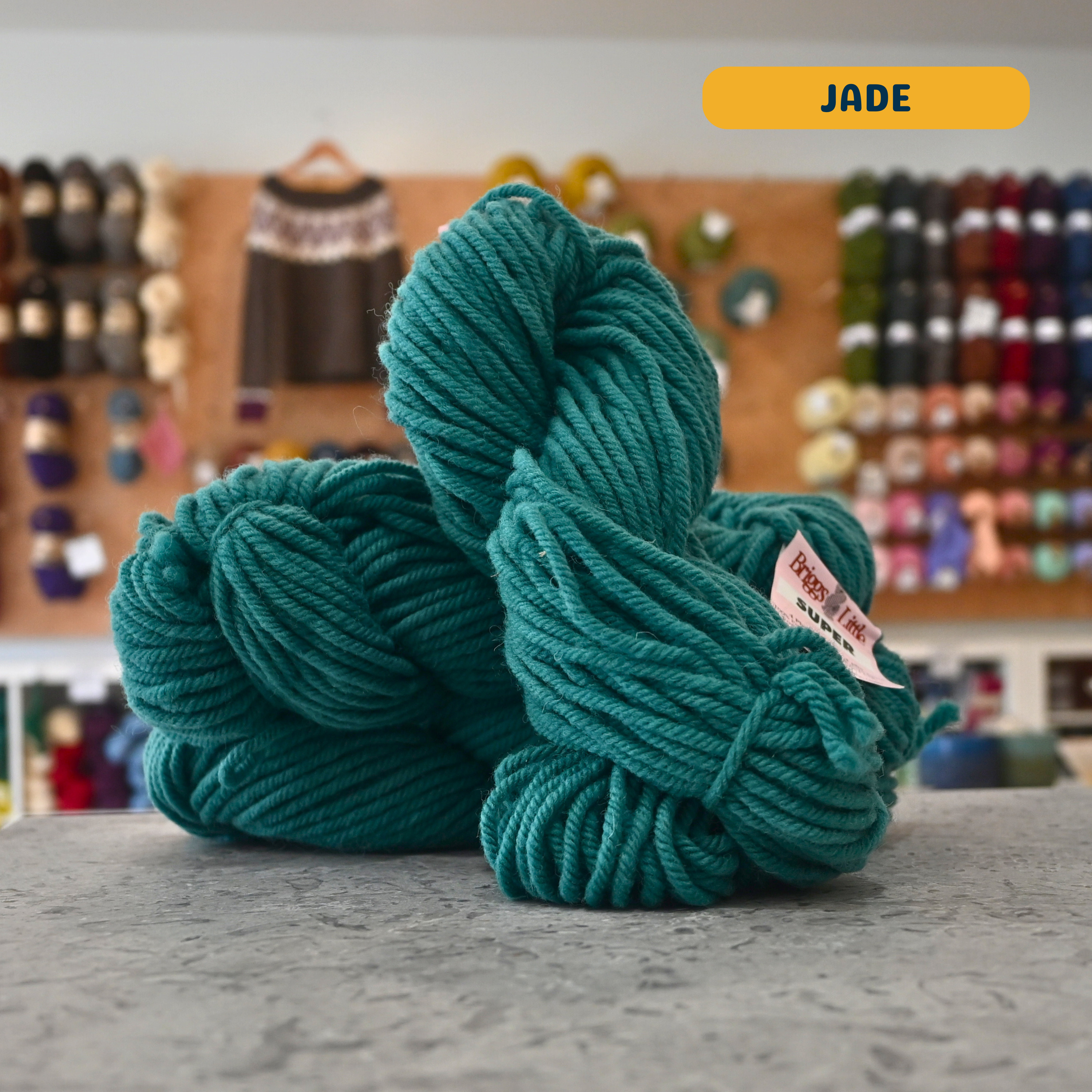 113g teal (jade) Canadian wool super bulky skein, Briggs & Little yarn, craft shop background (blurred)