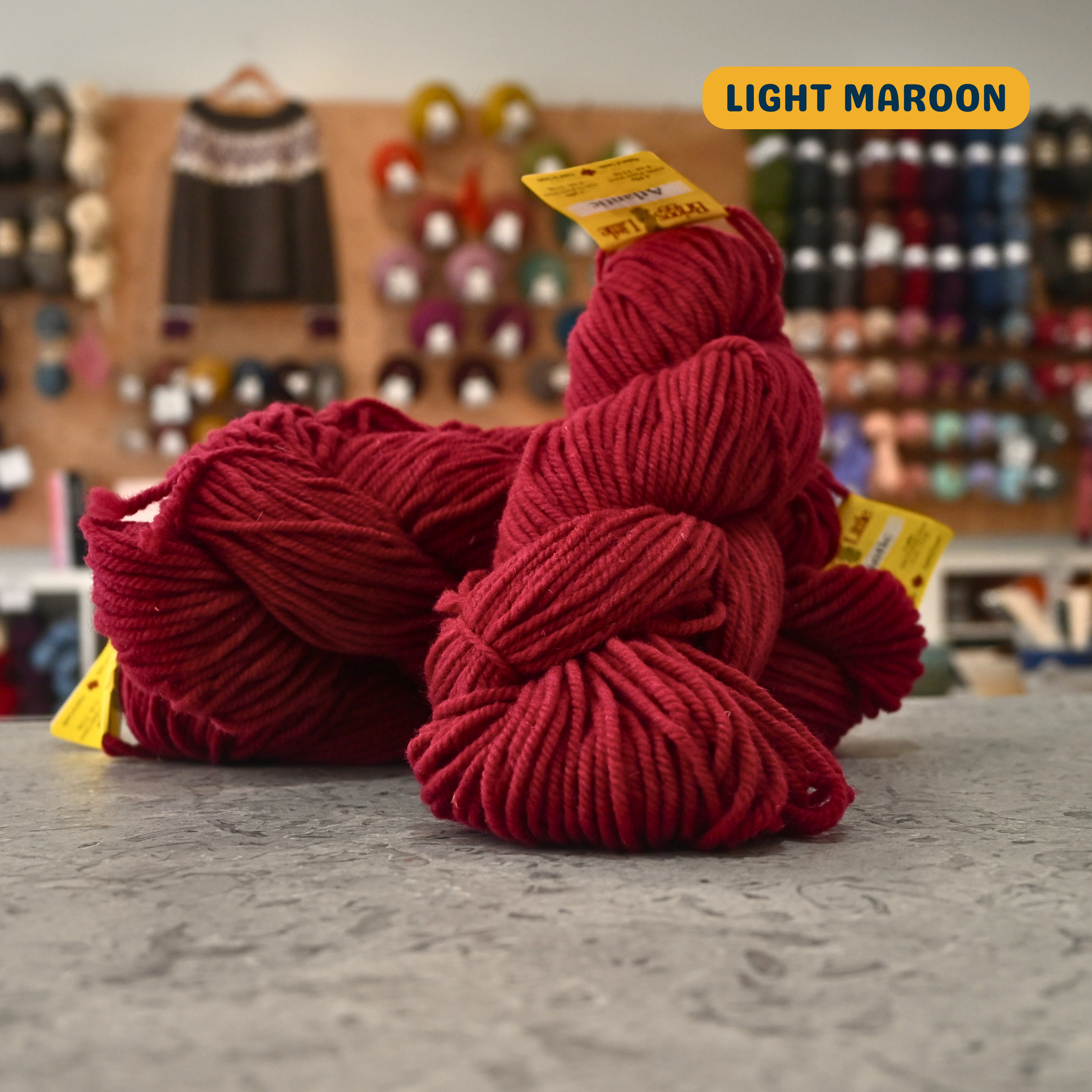 113g red (light maroon) Canadian wool bulky skein, Briggs & Little yarn, craft shop background (blurred)