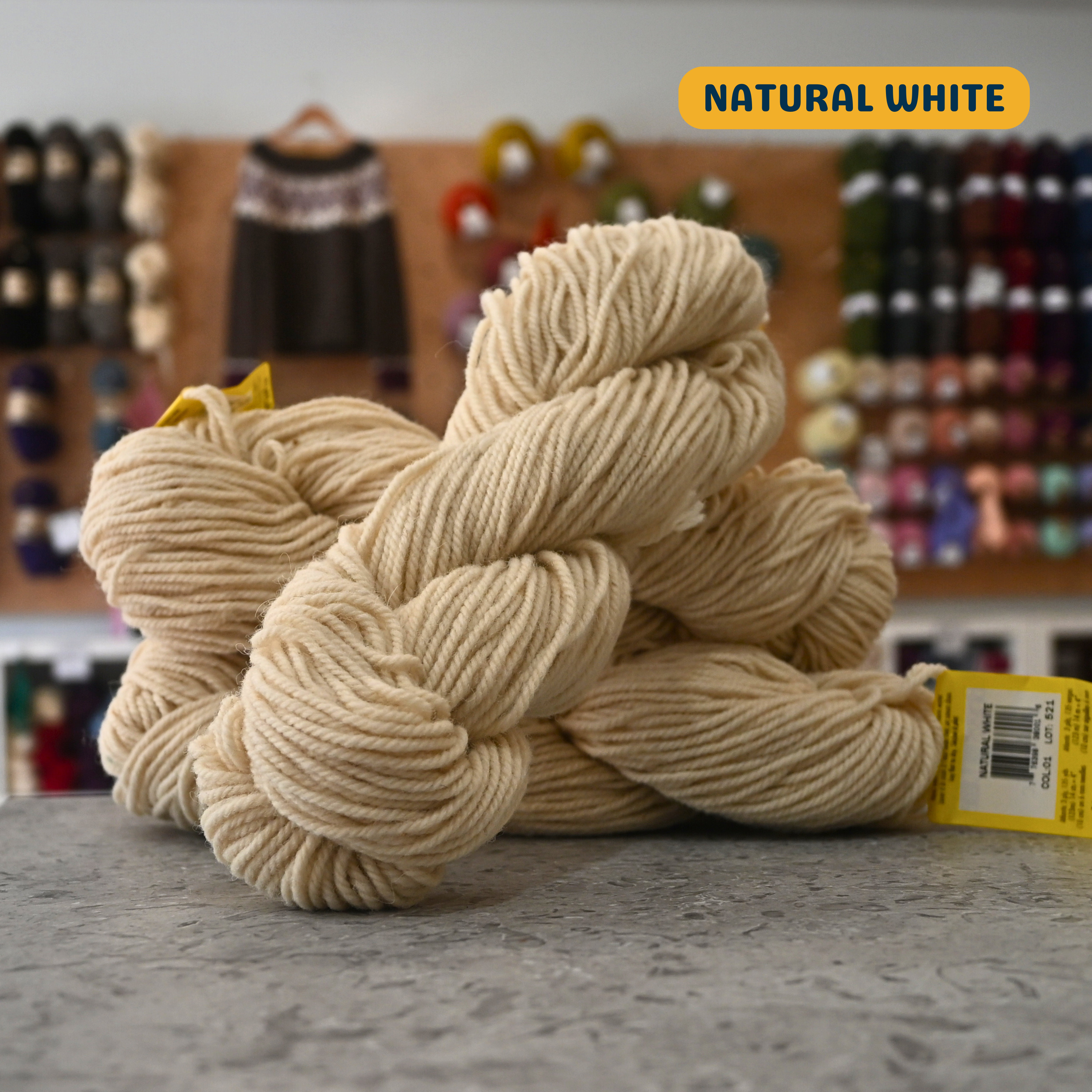 113g natural white Canadian wool bulky skein, Briggs & Little yarn, craft shop background (blurred)