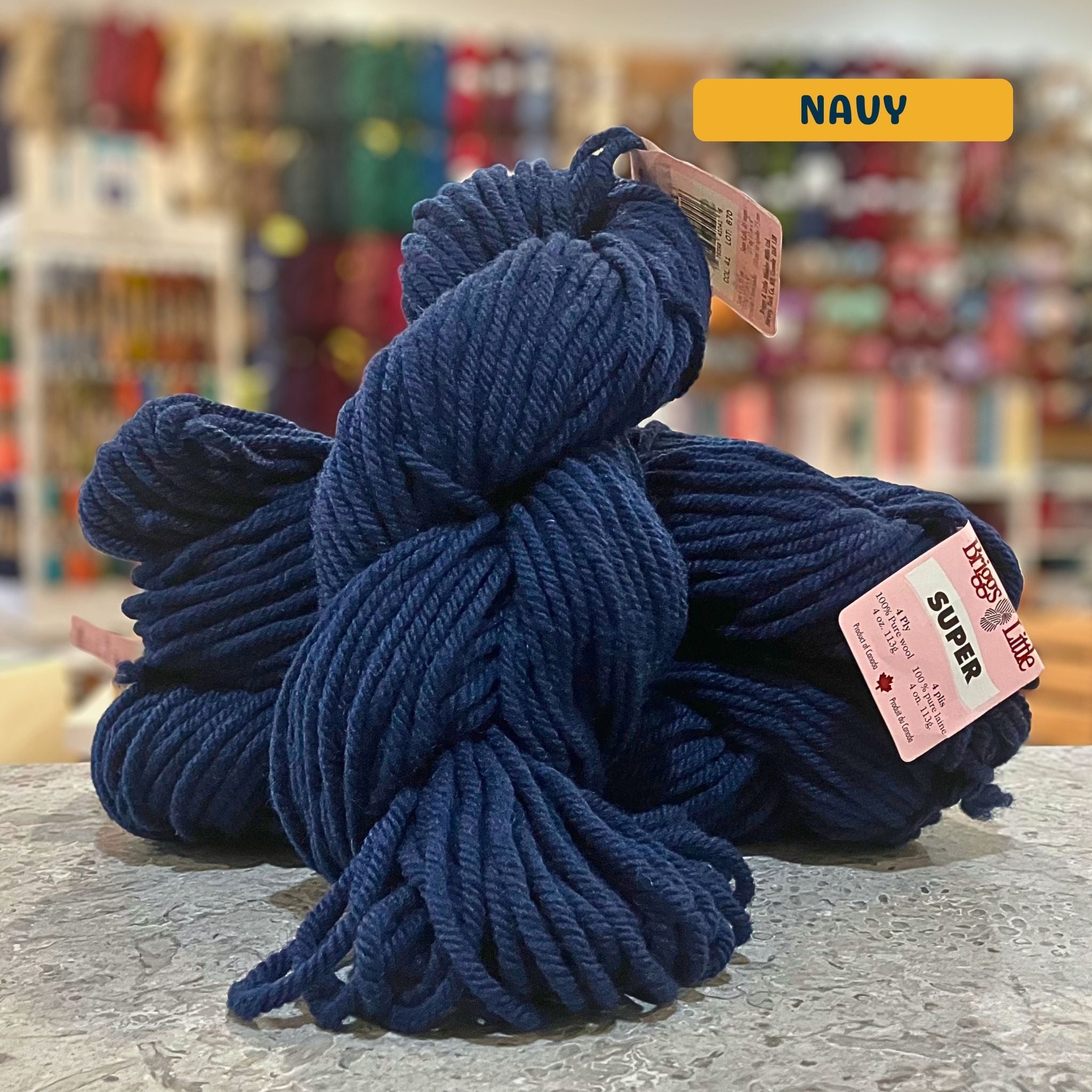 113g dark blue (navy) Canadian wool super bulky skein, Briggs & Little yarn, craft shop background (blurred)