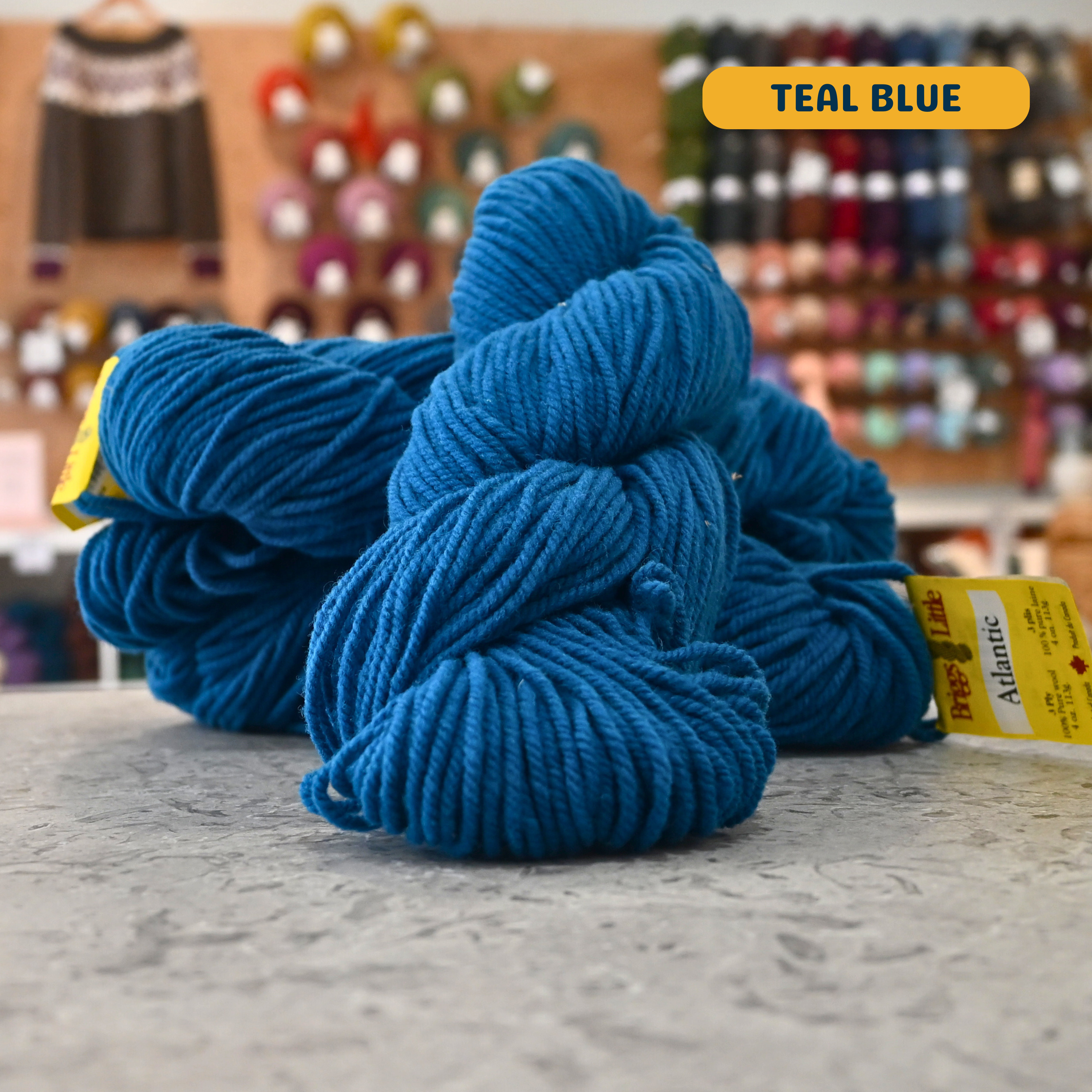 113g vibrant blue (teal) Canadian wool bulky skein, Briggs & Little yarn, craft shop background (blurred)
