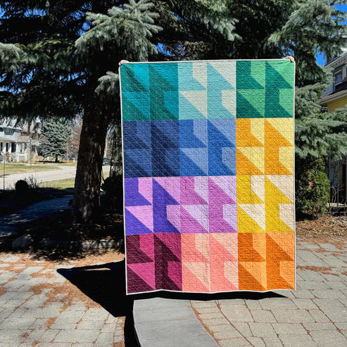 Colourful quilt with geometric pattern displayed outdoors against a tree
