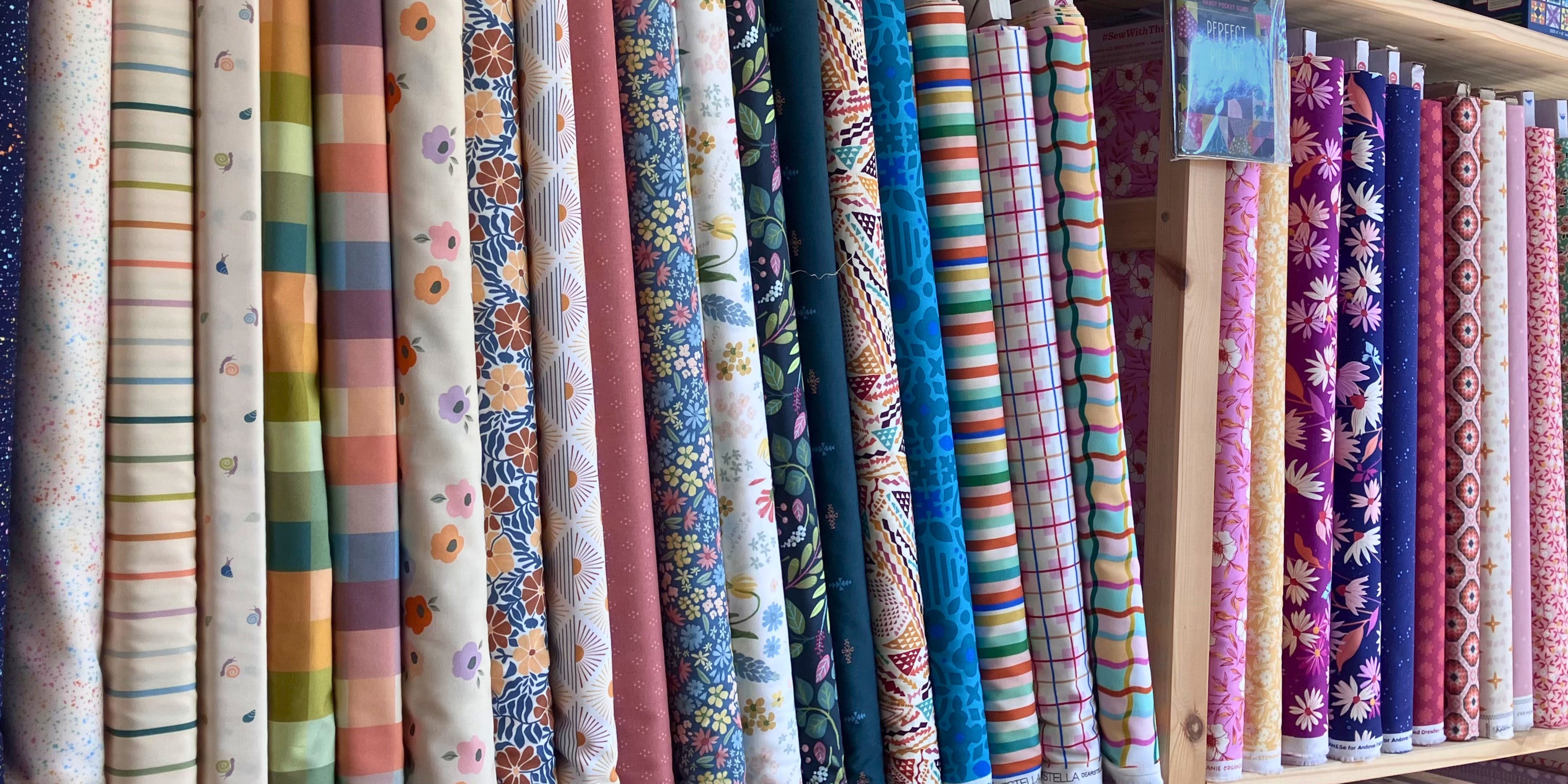 Row of colourful fabric bolts on shelf. 100% cotton. Colourful prints. Quilting fabrics.