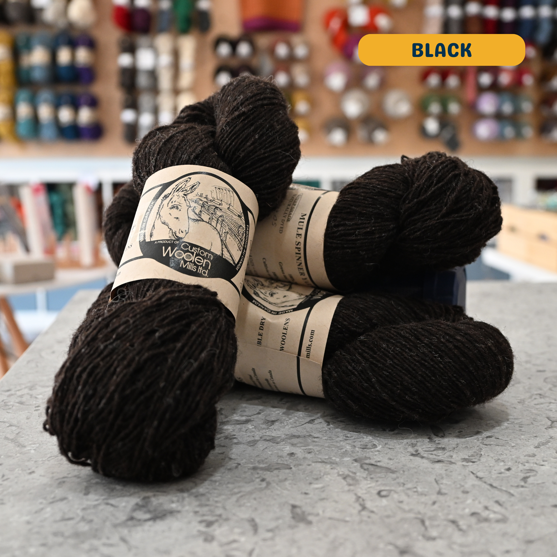 113g natural undyed brown-black Canadian wool fingering yarn, 'Custom Woolen Mills' label visible, craft shop background (blurred)