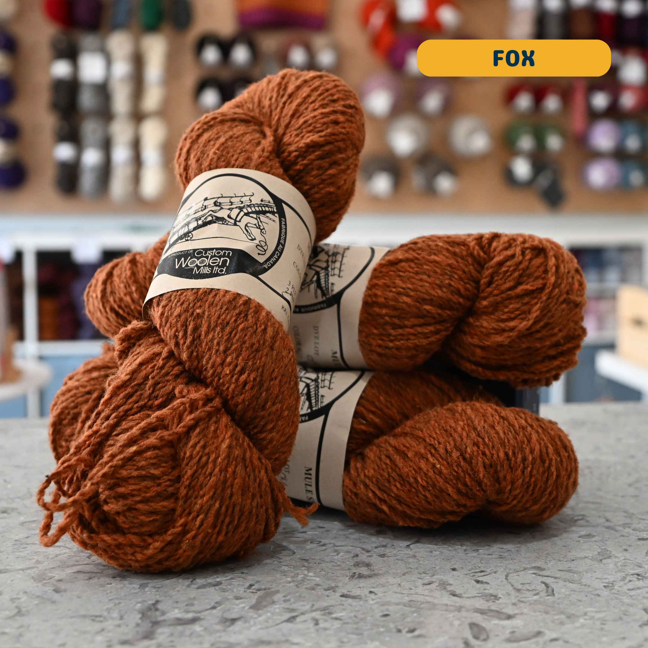 112g orange (fox) Canadian wool worsted yarn, 'Custom Woolen Mills' label visible, craft shop background (blurred)
