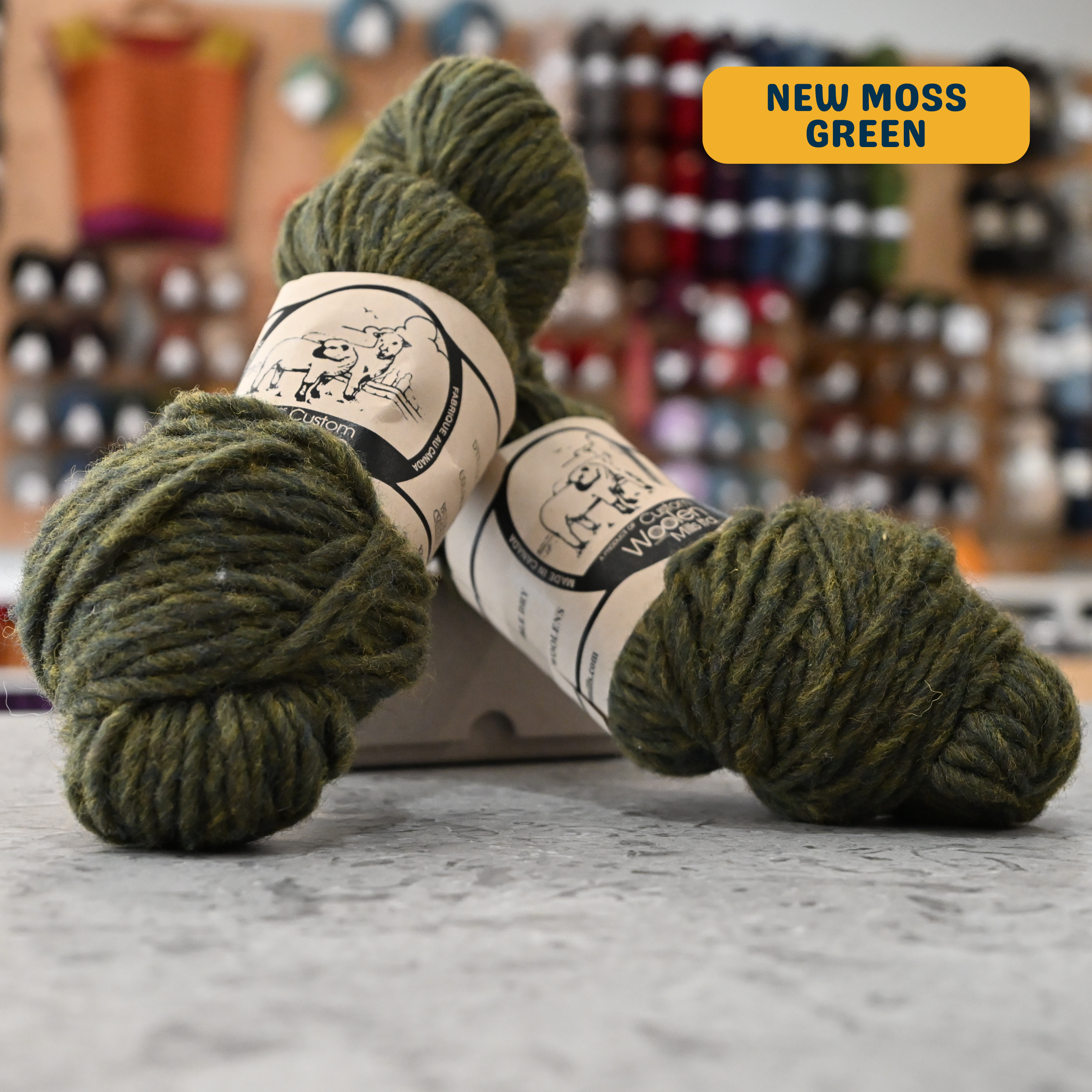 112g new moss green Canadian wool bulky yarn, 'Custom Woolen Mills' label visible, craft shop background (blurred)
