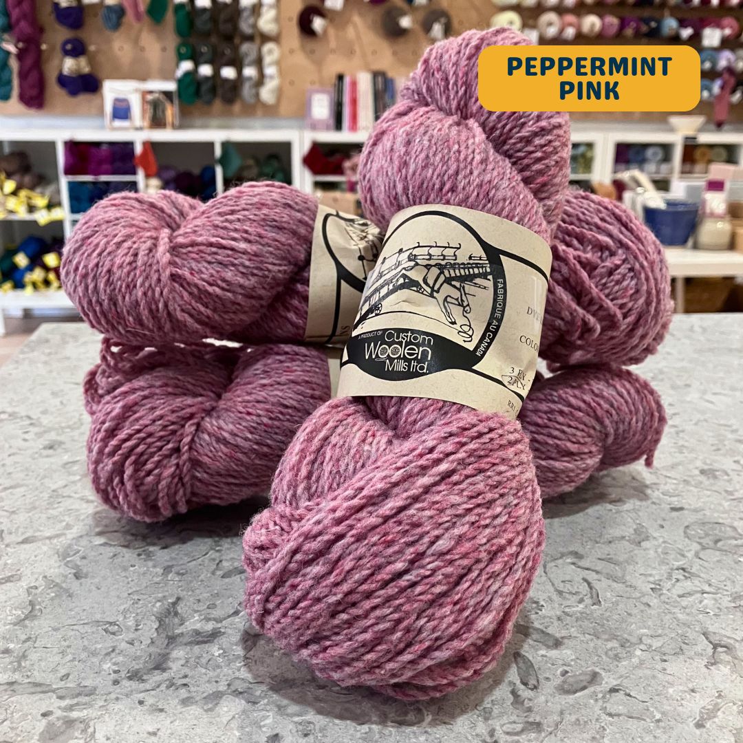 112g medium pink (peppermint pink)  Canadian wool worsted yarn, 'Custom Woolen Mills' label visible, craft shop background (blurred)
