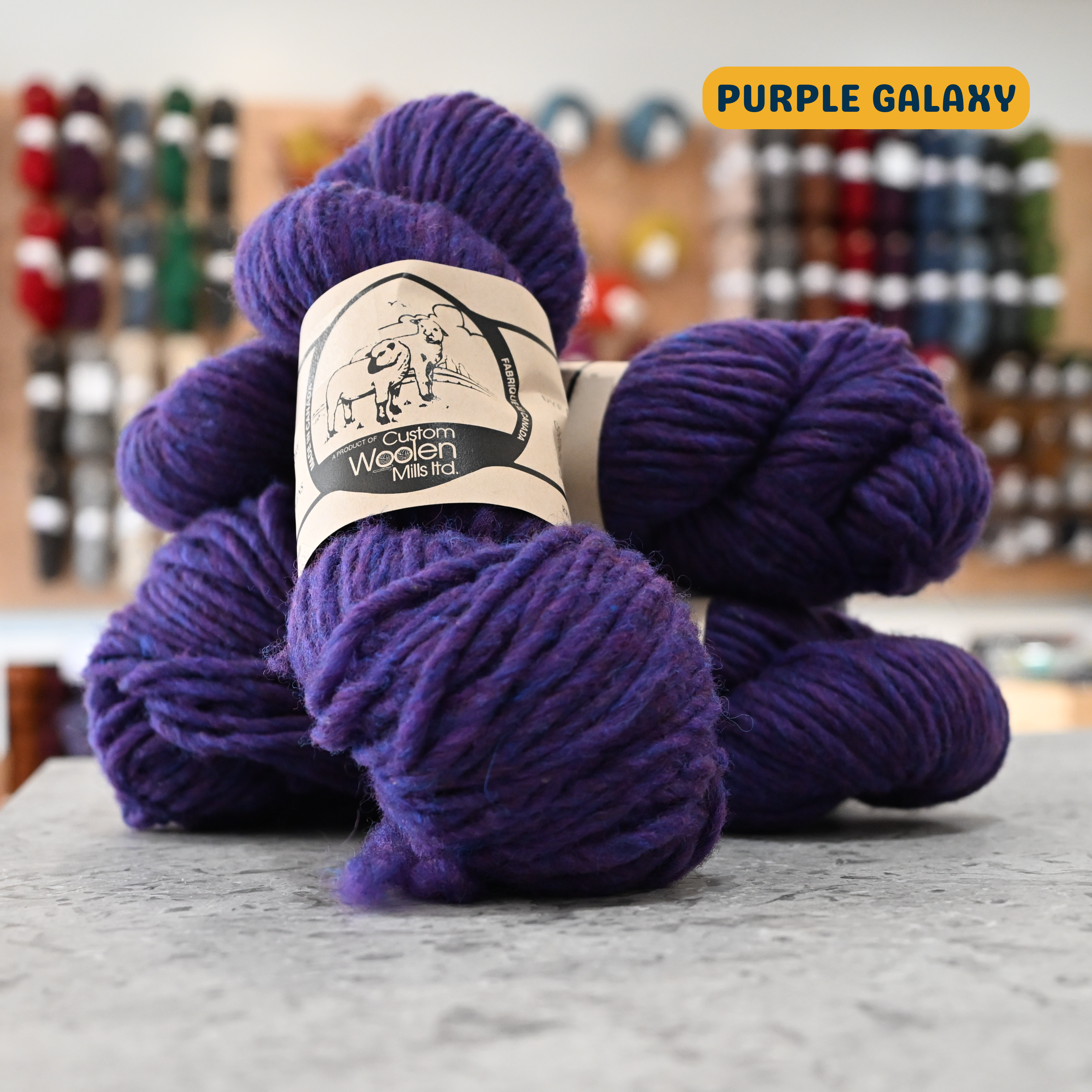 112g blue-purple (purple galaxy) Canadian wool bulky yarn, 'Custom Woolen Mills' label visible, craft shop background (blurred)