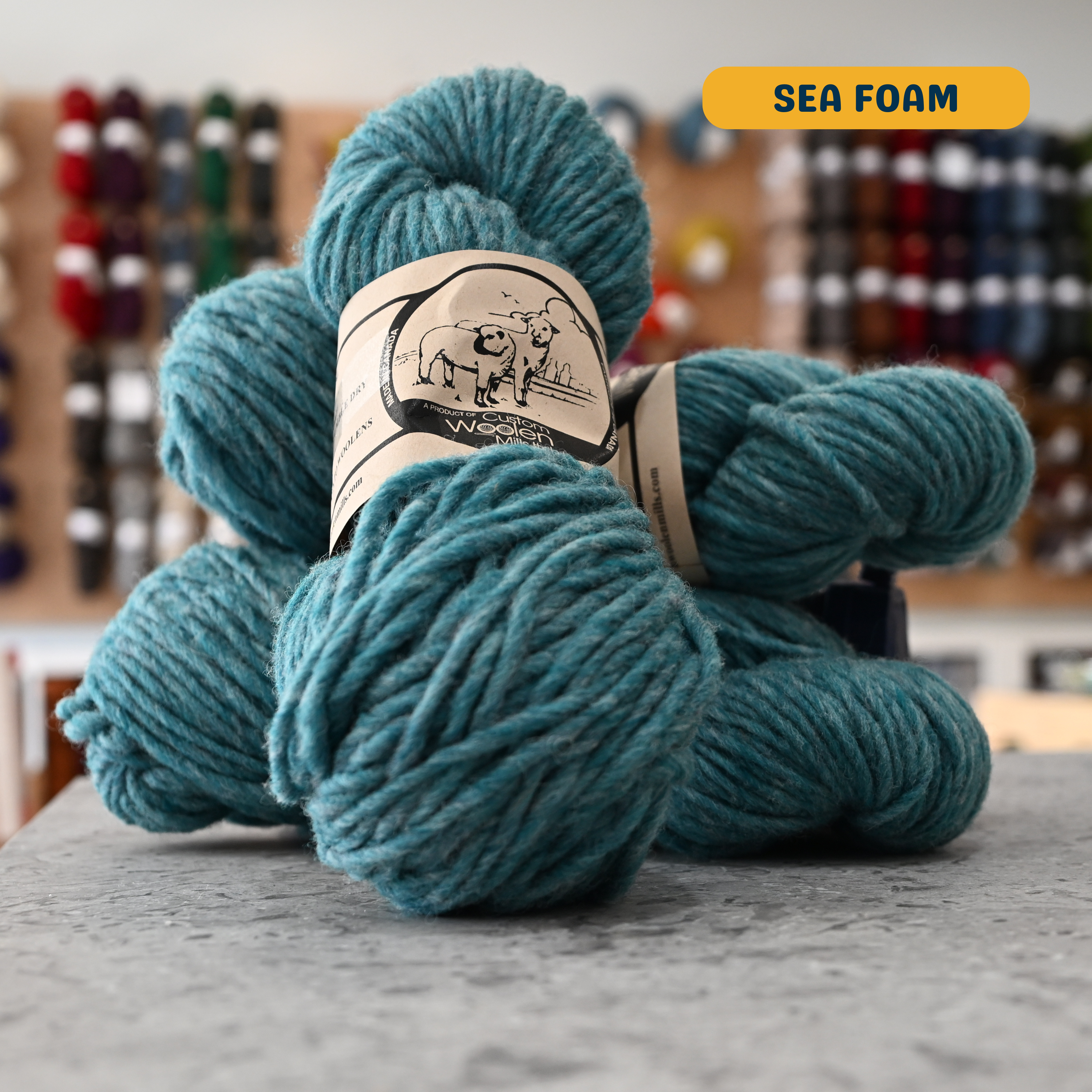 112g teal (sea foam) Canadian wool bulky yarn, 'Custom Woolen Mills' label visible, craft shop background (blurred)
