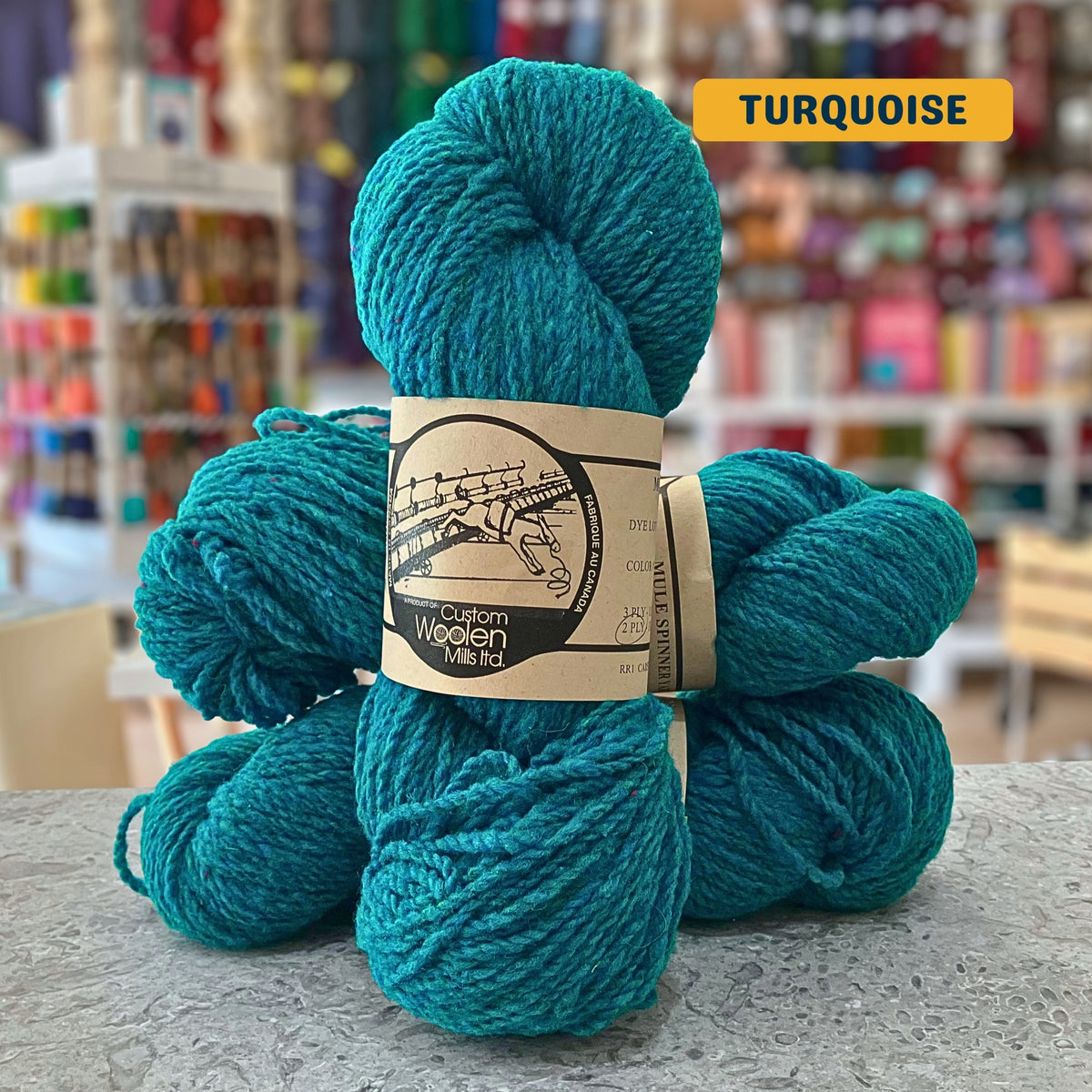 112g green-blue (turquoise)  Canadian wool worsted yarn, 'Custom Woolen Mills' label visible, craft shop background (blurred)