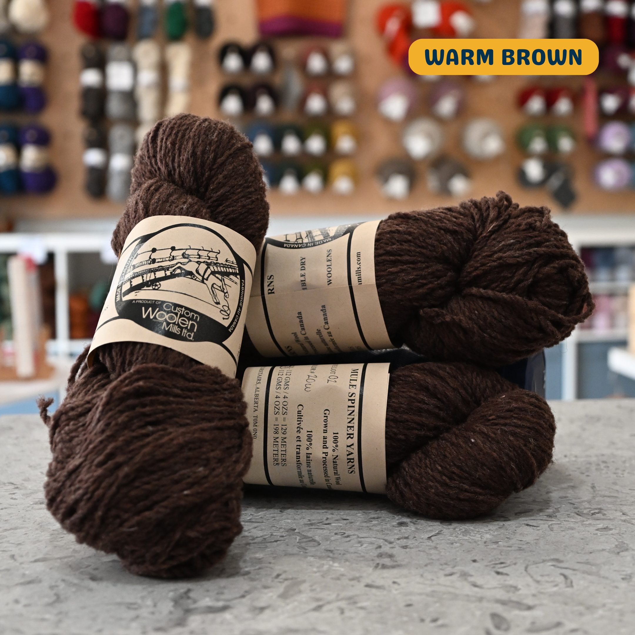 112g warm brown Canadian wool worsted yarn, 'Custom Woolen Mills' label visible, craft shop background (blurred)