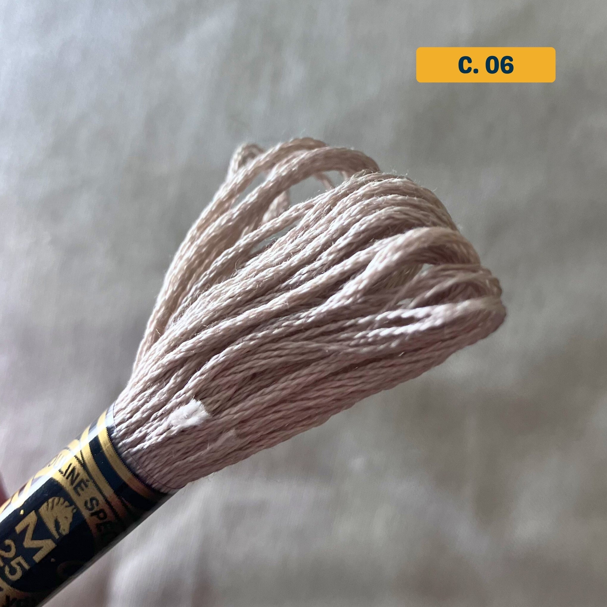 DMC 6-Strand Cotton Embroidery Floss – 06 Light Beige – 8m skein, 100% Egyptian cotton. Fabric background (blurred).