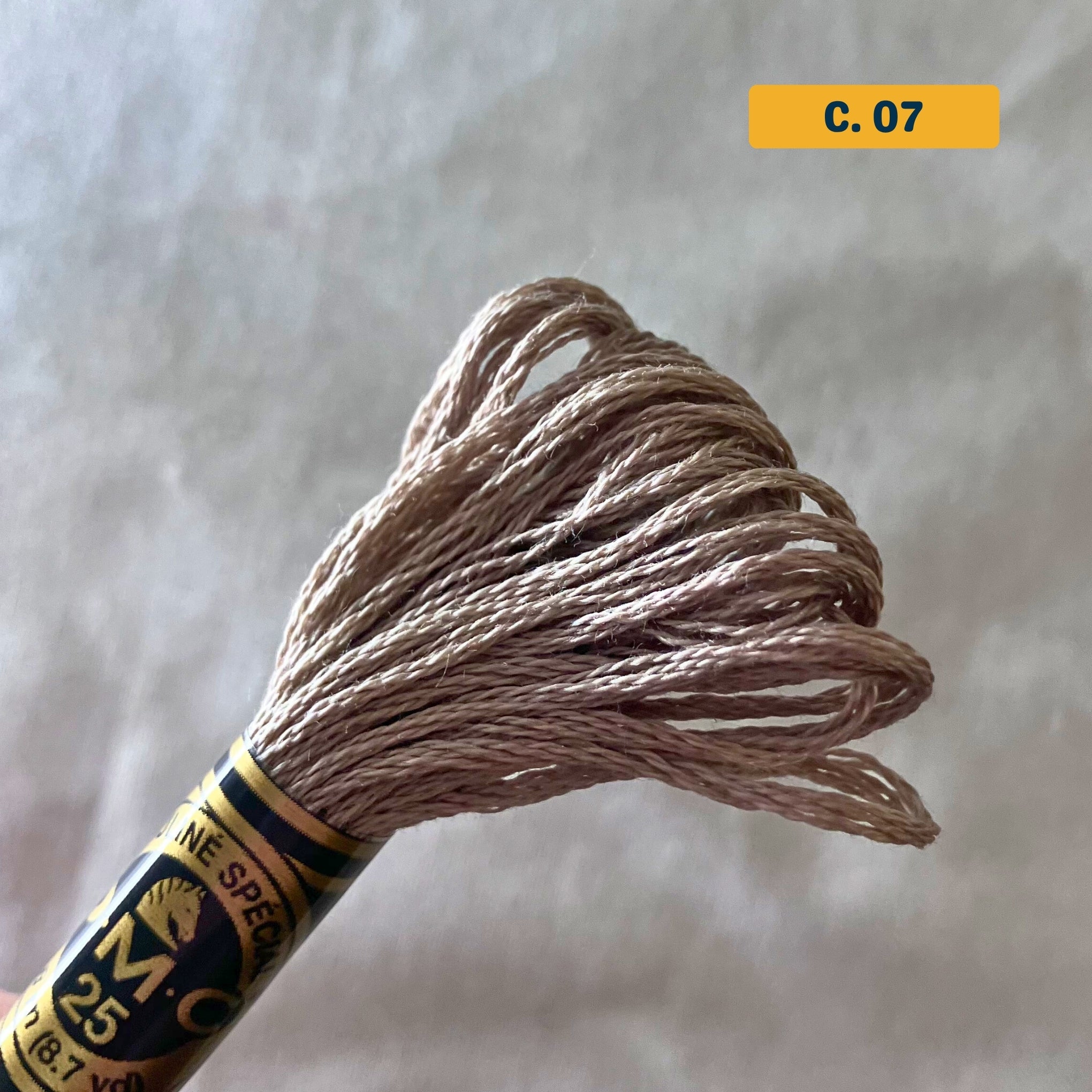 DMC 6-Strand Cotton Embroidery Floss – 07 Beige – 8m skein, 100% Egyptian cotton. Fabric background (blurred).