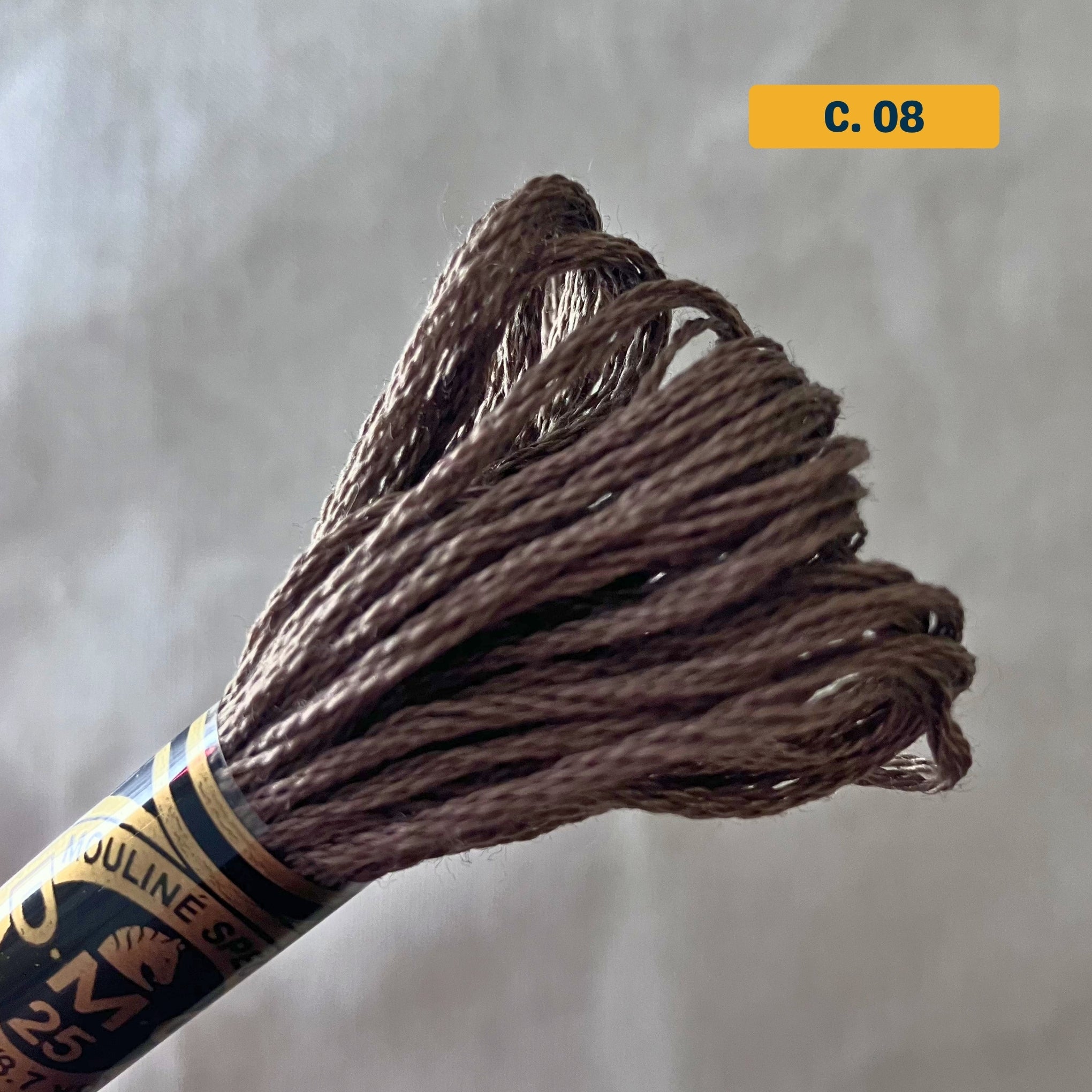 DMC 6-Strand Cotton Embroidery Floss – 08 Brown – 8m skein, 100% Egyptian cotton. Fabric background (blurred).