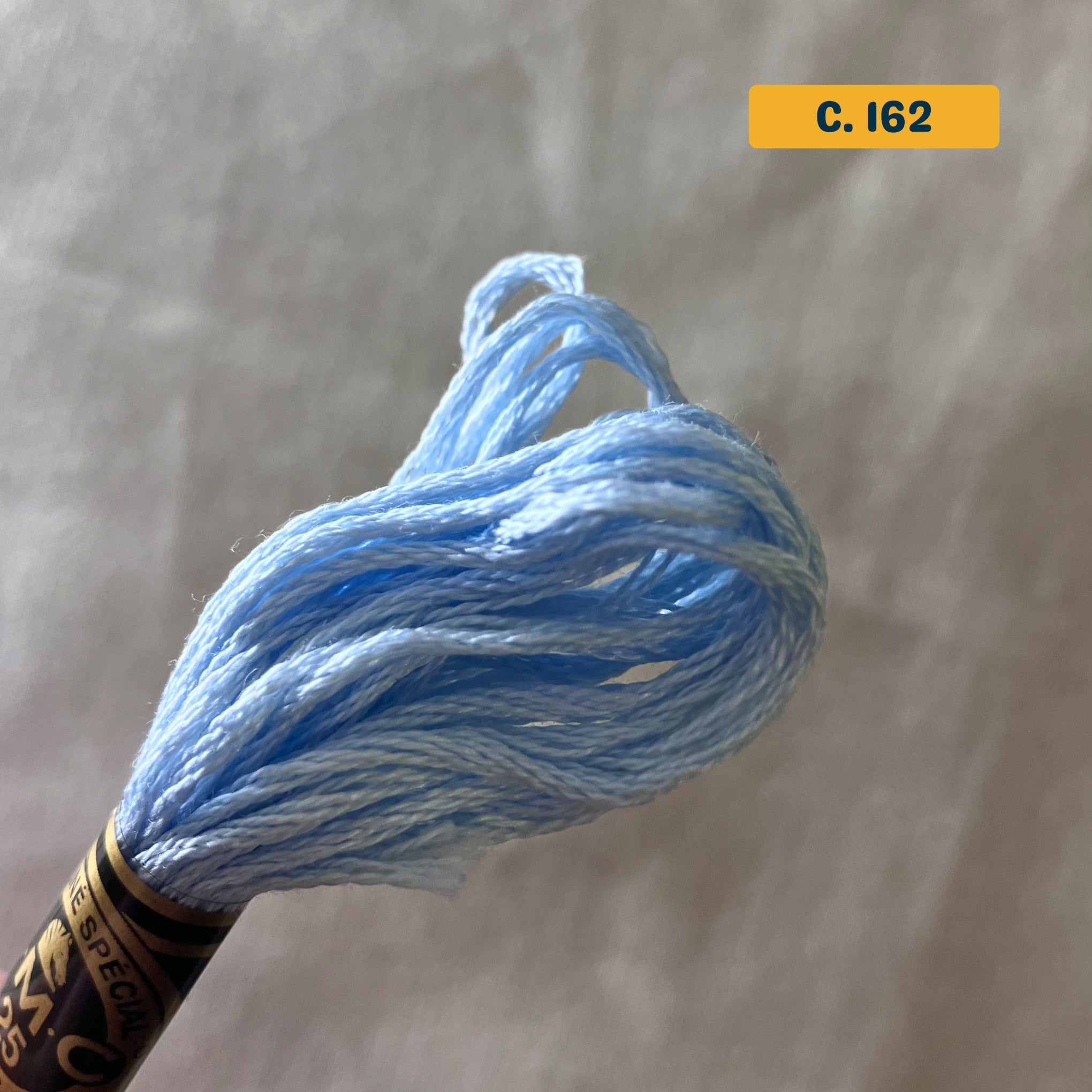 DMC 6-Strand Cotton Embroidery Floss – 162 Sky Blue – 8m skein, 100% Egyptian cotton. Fabric background (blurred).