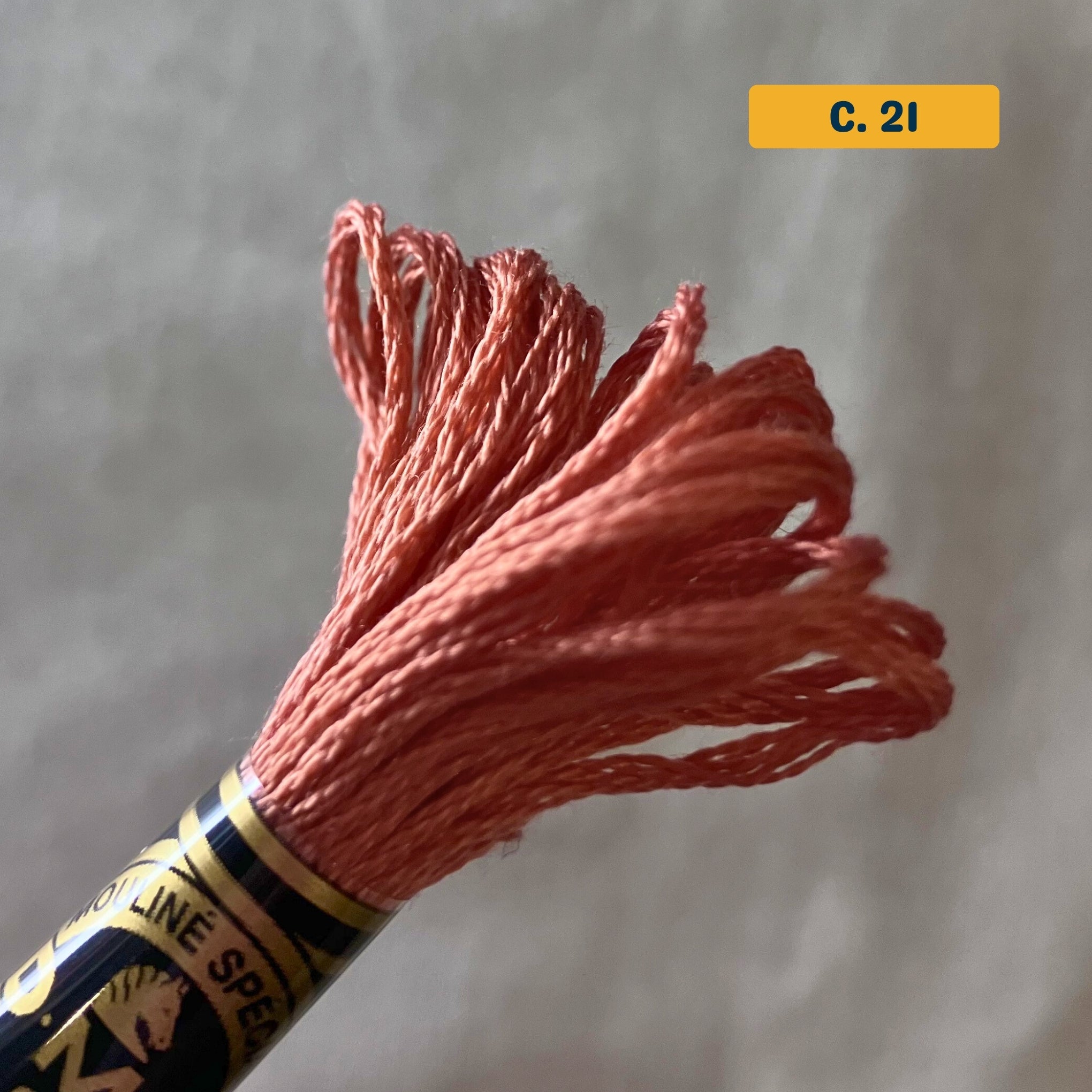 DMC 6-Strand Cotton Embroidery Floss – 21 Coral – 8m skein, 100% Egyptian cotton. Fabric background (blurred).