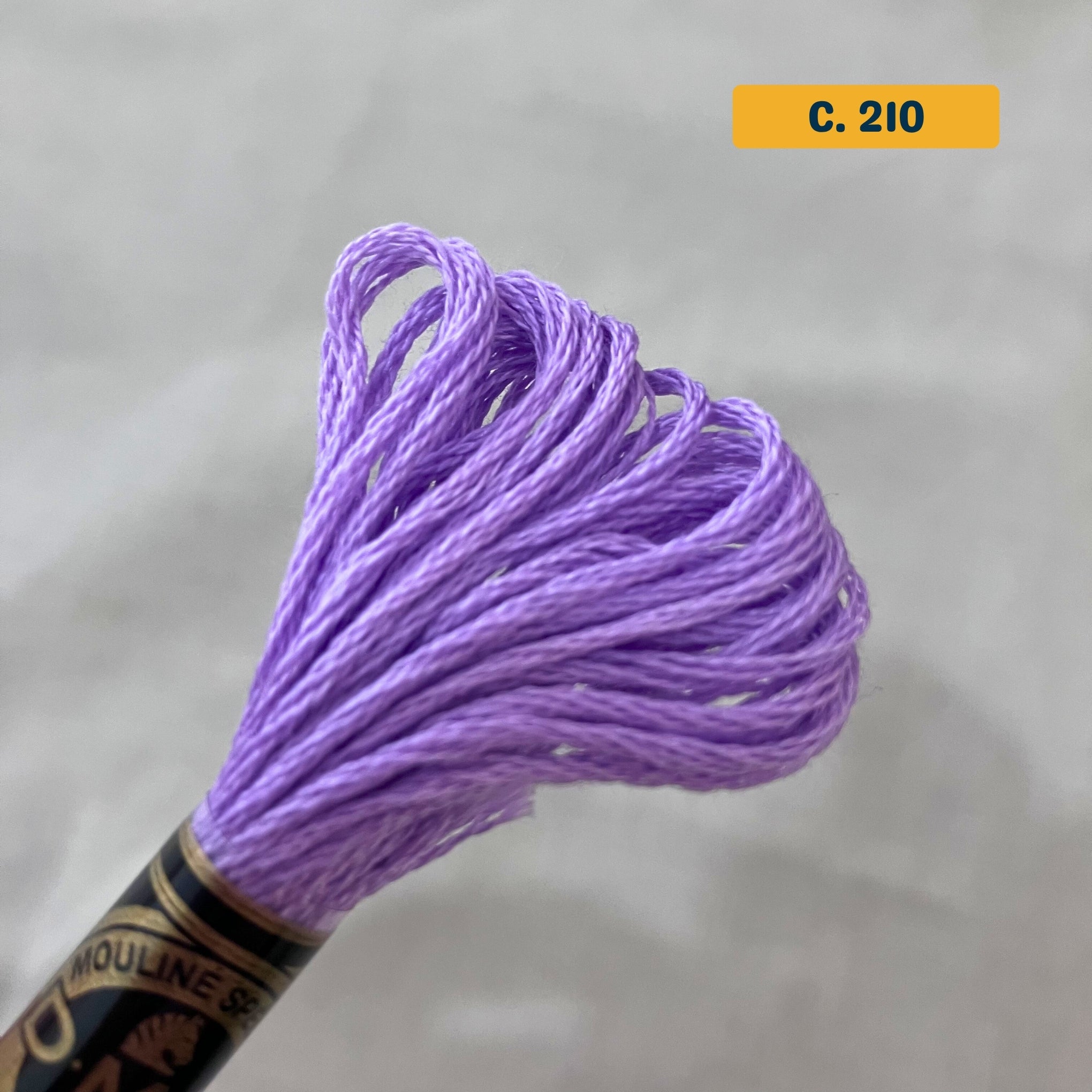 DMC 6-Strand Cotton Embroidery Floss – 210 Lilac – 8m skein, 100% Egyptian cotton. Fabric background (blurred).