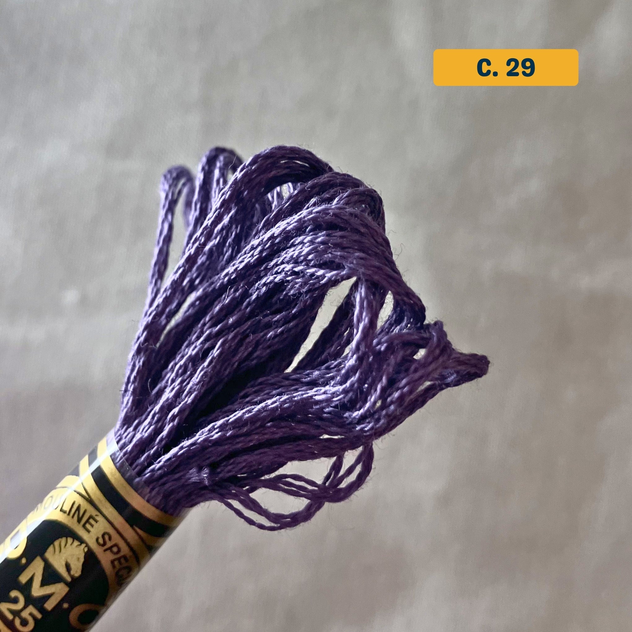 DMC 6-Strand Cotton Embroidery Floss – 29 Eggplant  – 8m skein, 100% Egyptian cotton. Fabric background (blurred).