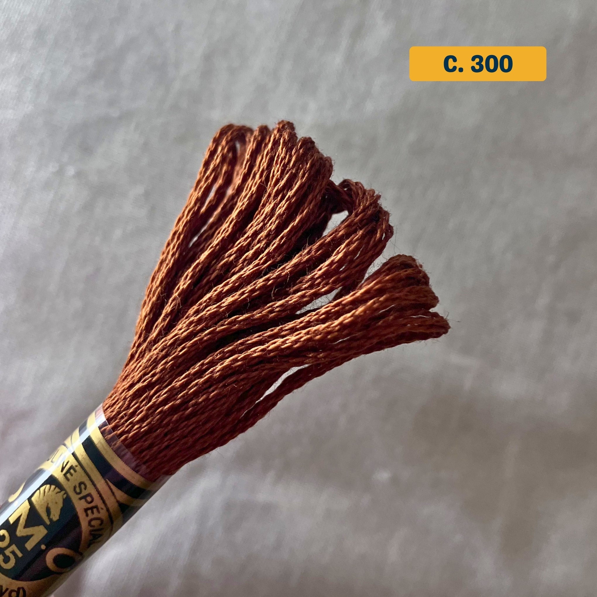 DMC 6-Strand Cotton Embroidery Floss – 300 Medium Copper – 8m skein, 100% Egyptian cotton. Fabric background (blurred).