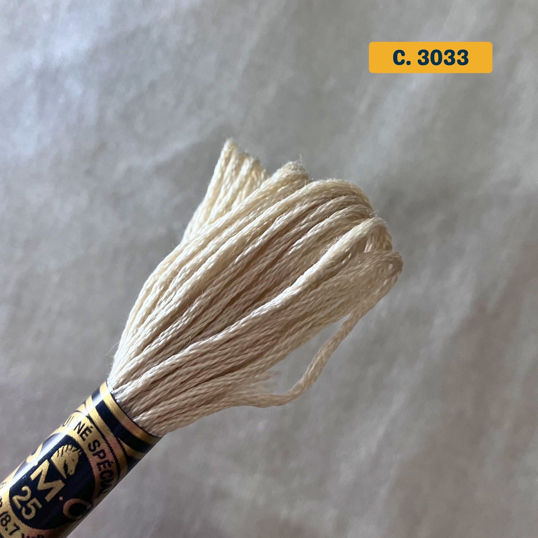 DMC 6-Strand Cotton Embroidery Floss – 3033 Natural – 8m skein, 100% Egyptian cotton. Fabric background (blurred).