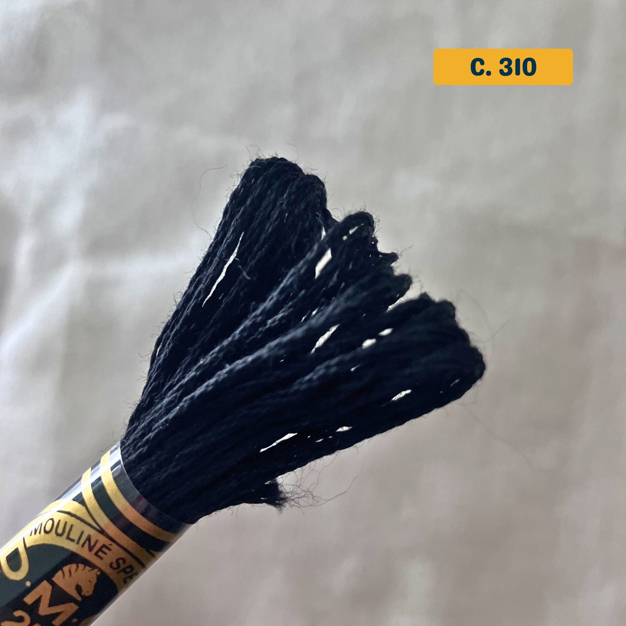 DMC 6-Strand Cotton Embroidery Floss – 310 Black – 8m skein, 100% Egyptian cotton. Fabric background (blurred).