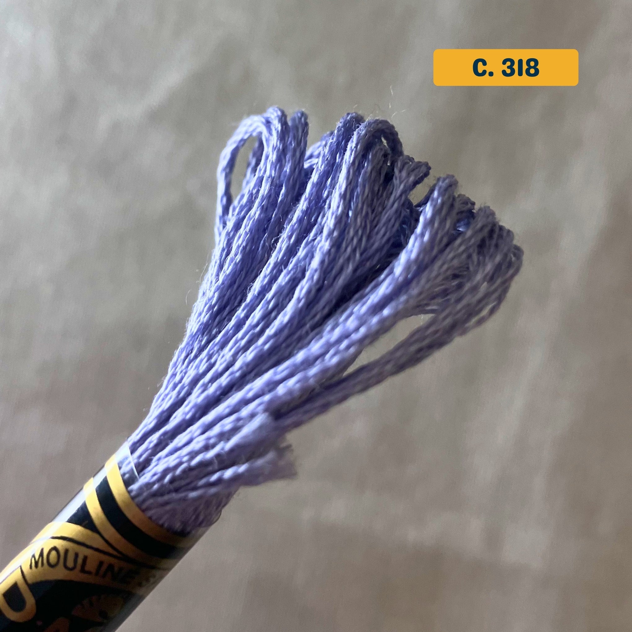 DMC 6-Strand Cotton Embroidery Floss – 318 Purple-Blue – 8m skein, 100% Egyptian cotton. Fabric background (blurred).