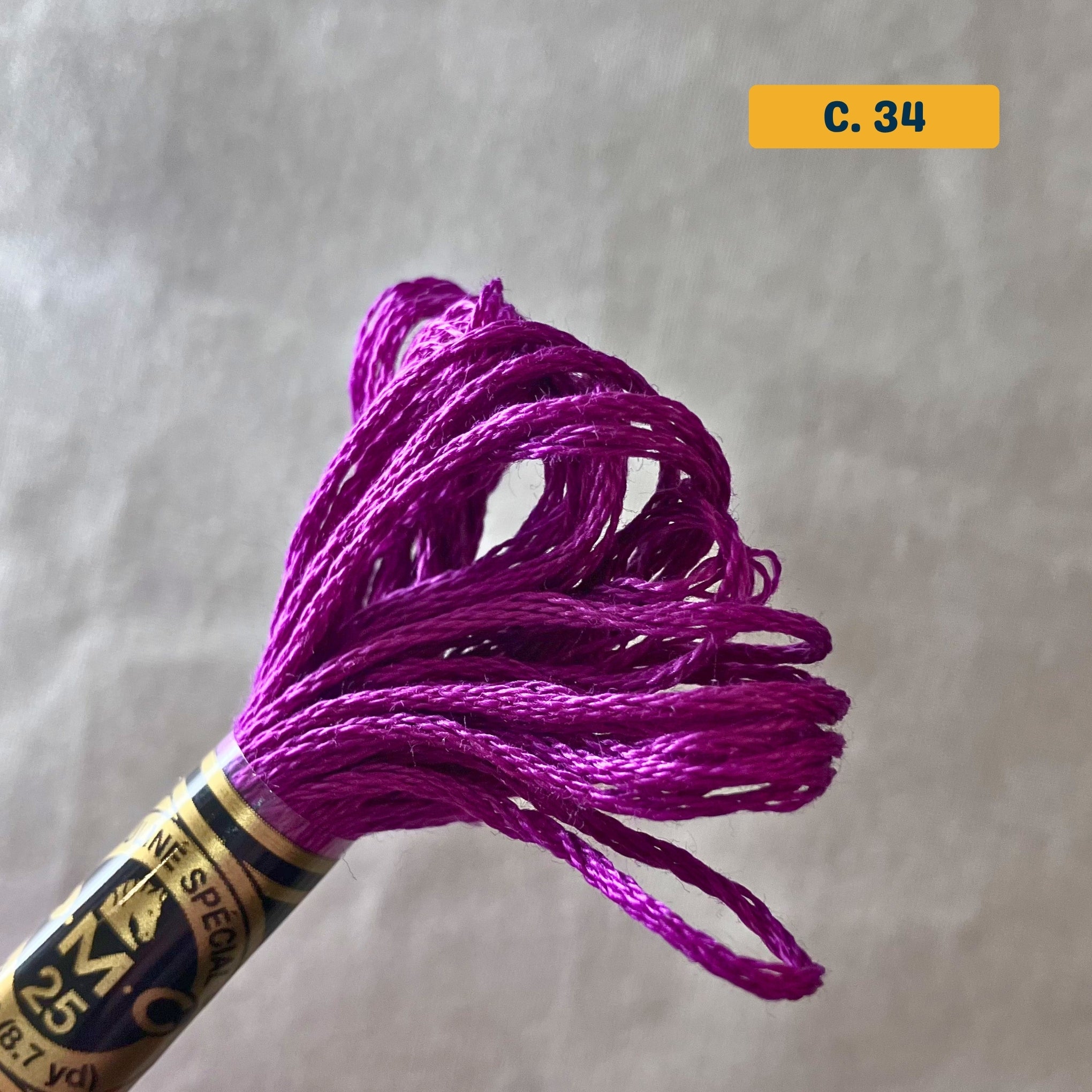 DMC 6-Strand Cotton Embroidery Floss – 34 Magenta – 8m skein, 100% Egyptian cotton. Fabric background (blurred).