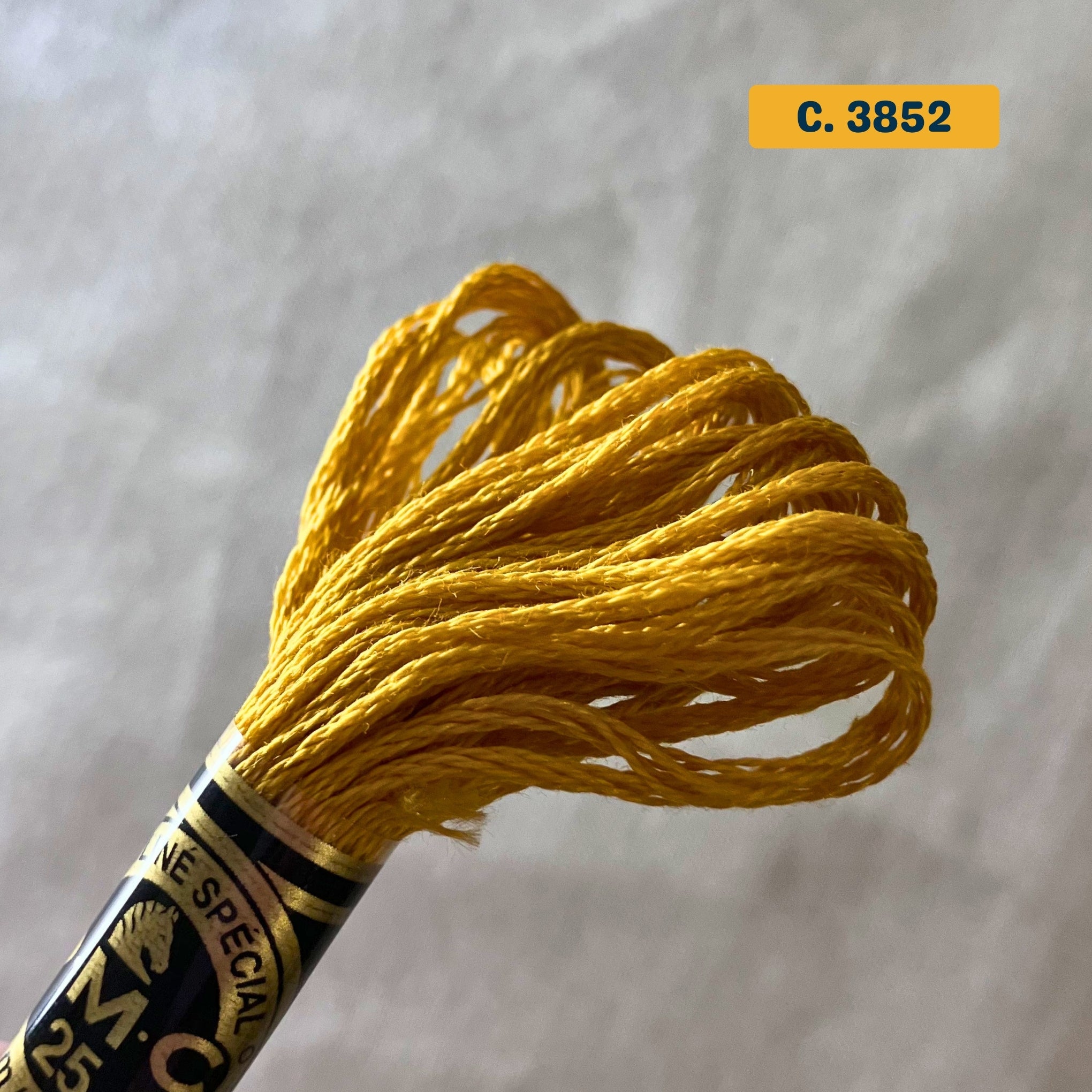 DMC 6-Strand Cotton Embroidery Floss – 3852 Golden Yellow – 8m skein, 100% Egyptian cotton. Fabric background (blurred).