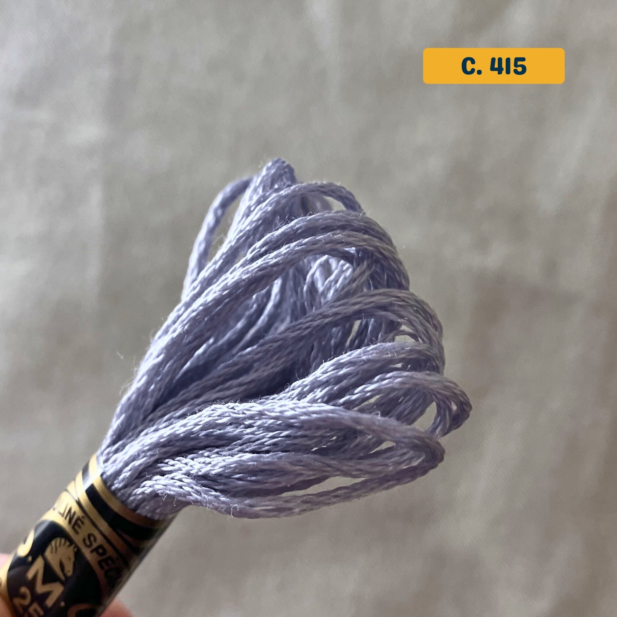 DMC 6-Strand Cotton Embroidery Floss – 415 Light Grey – 8m skein, 100% Egyptian cotton. Fabric background (blurred).