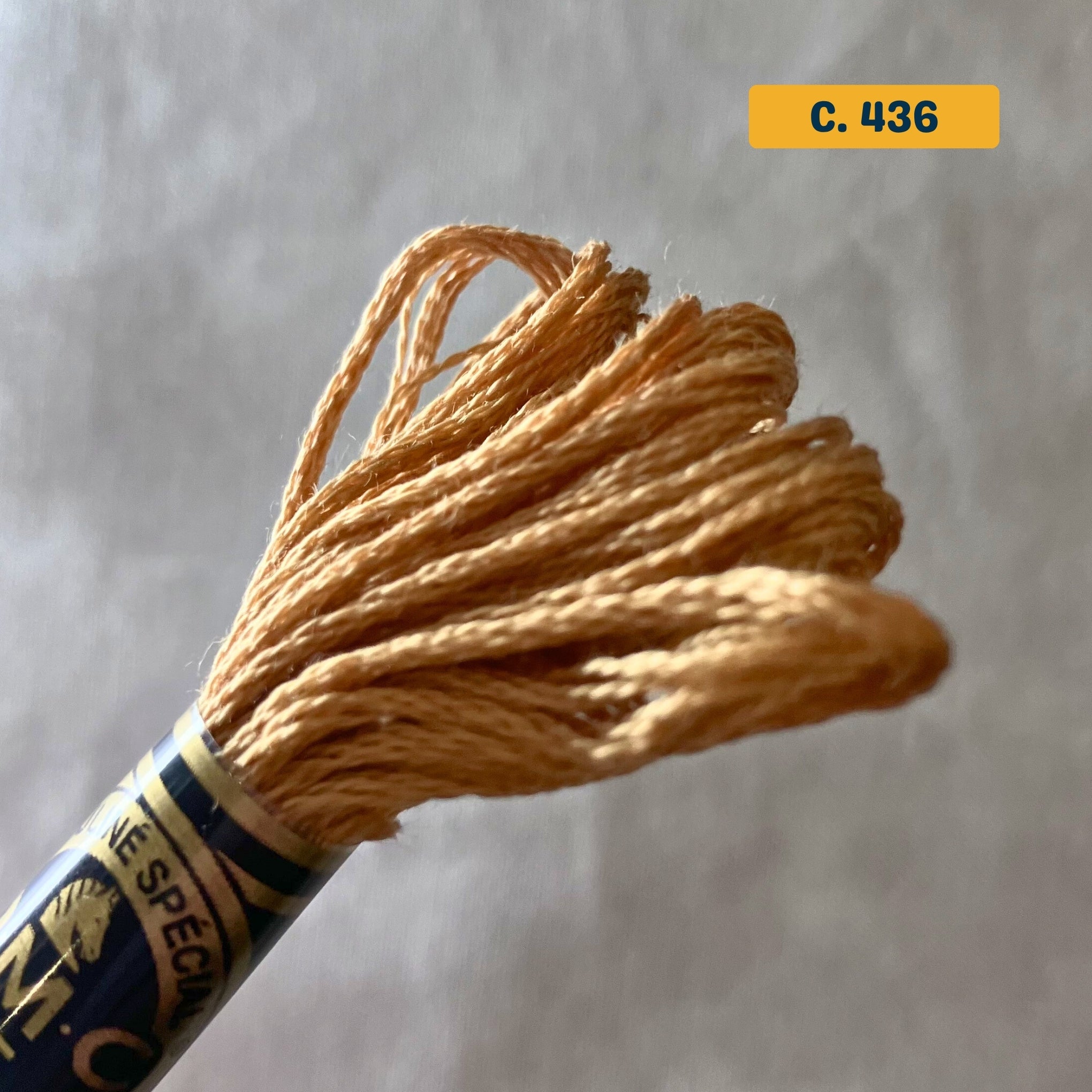 DMC 6-Strand Cotton Embroidery Floss – 436 Caramel Brown – 8m skein, 100% Egyptian cotton. Fabric background (blurred).