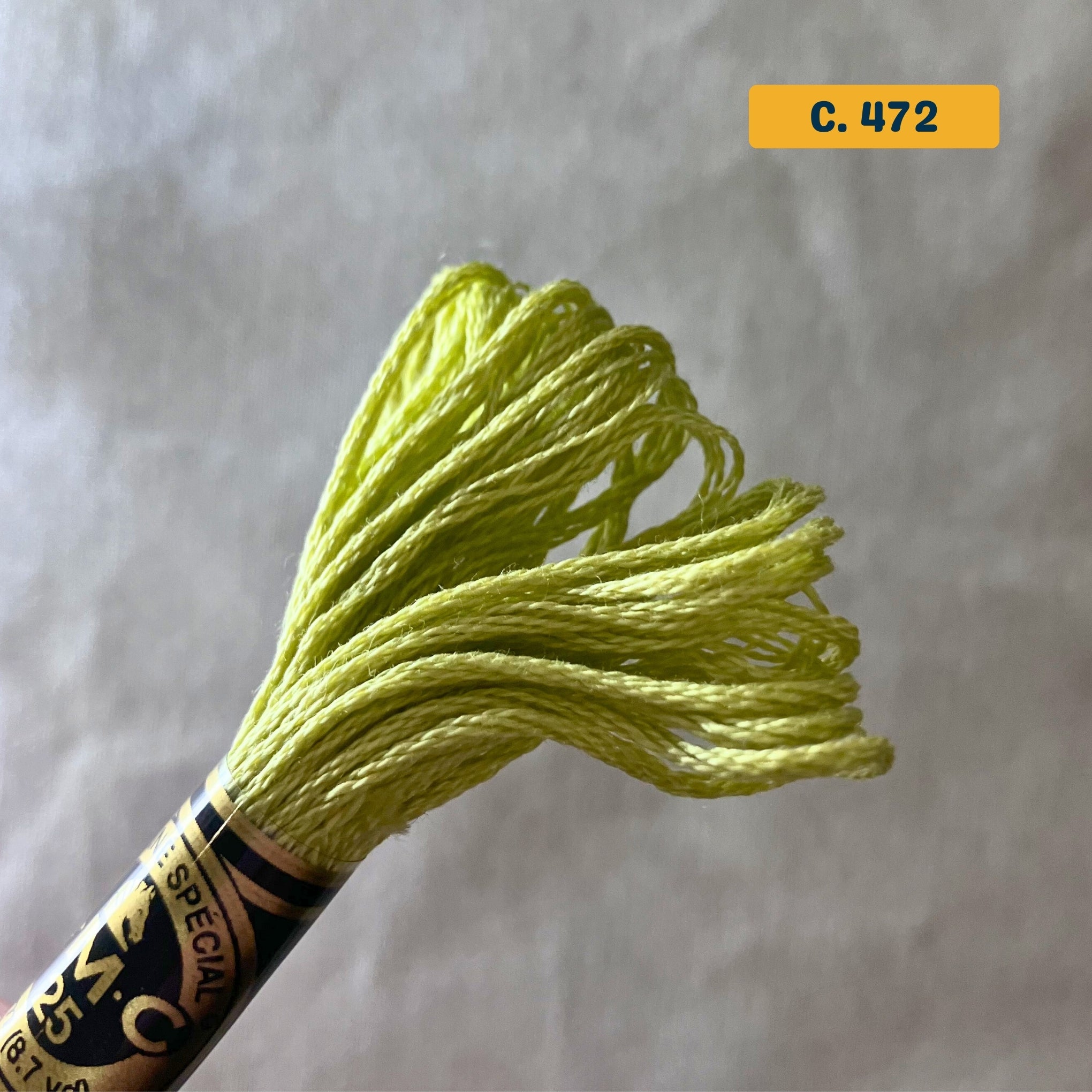 DMC 6-Strand Cotton Embroidery Floss – 472 Yellow-Green – 8m skein, 100% Egyptian cotton. Fabric background (blurred).