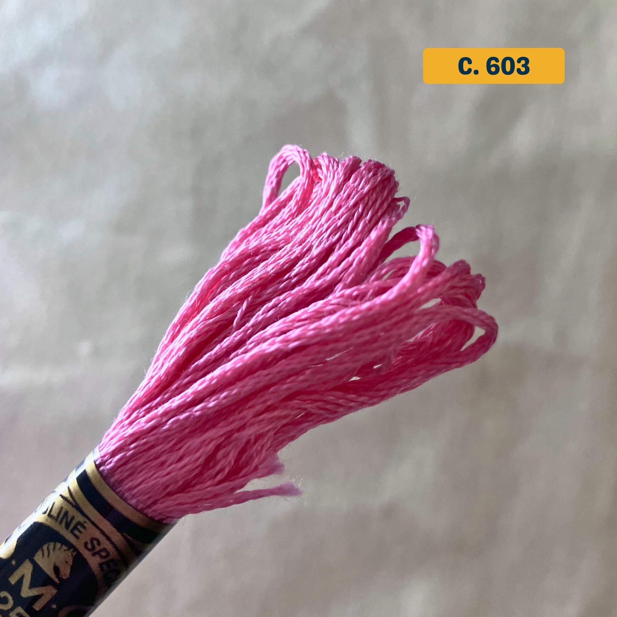 DMC 6-Strand Cotton Embroidery Floss – 603 Pink – 8m skein, 100% Egyptian cotton. Fabric background (blurred).