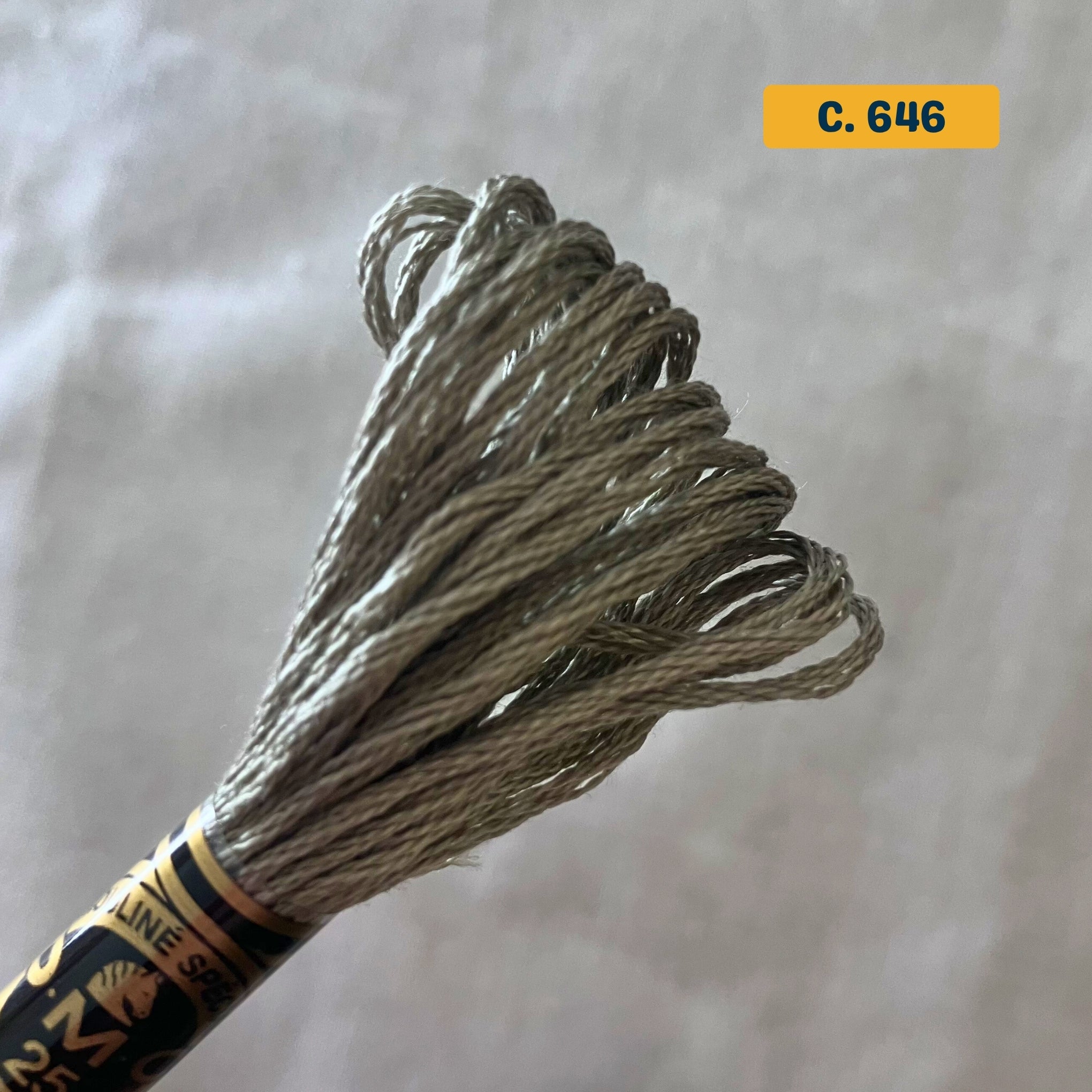 DMC 6-Strand Cotton Embroidery Floss – 646 Brown-Grey – 8m skein, 100% Egyptian cotton. Fabric background (blurred).