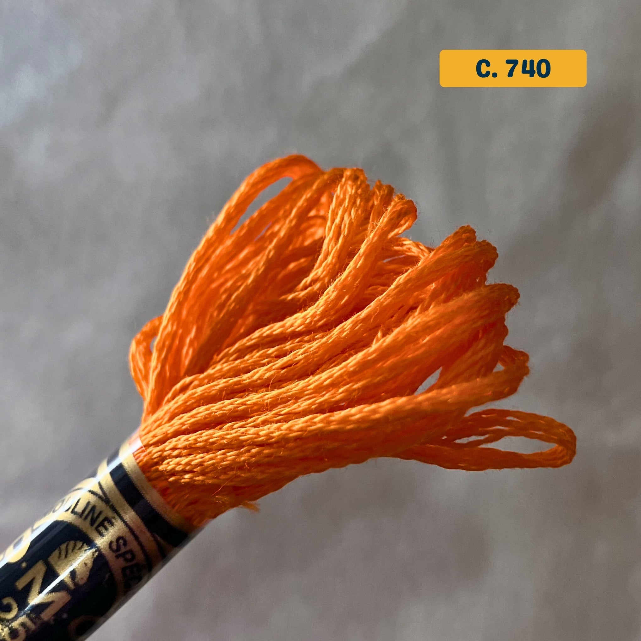 DMC 6-Strand Cotton Embroidery Floss – 740 Bright Orange – 8m skein, 100% Egyptian cotton. Fabric background (blurred).