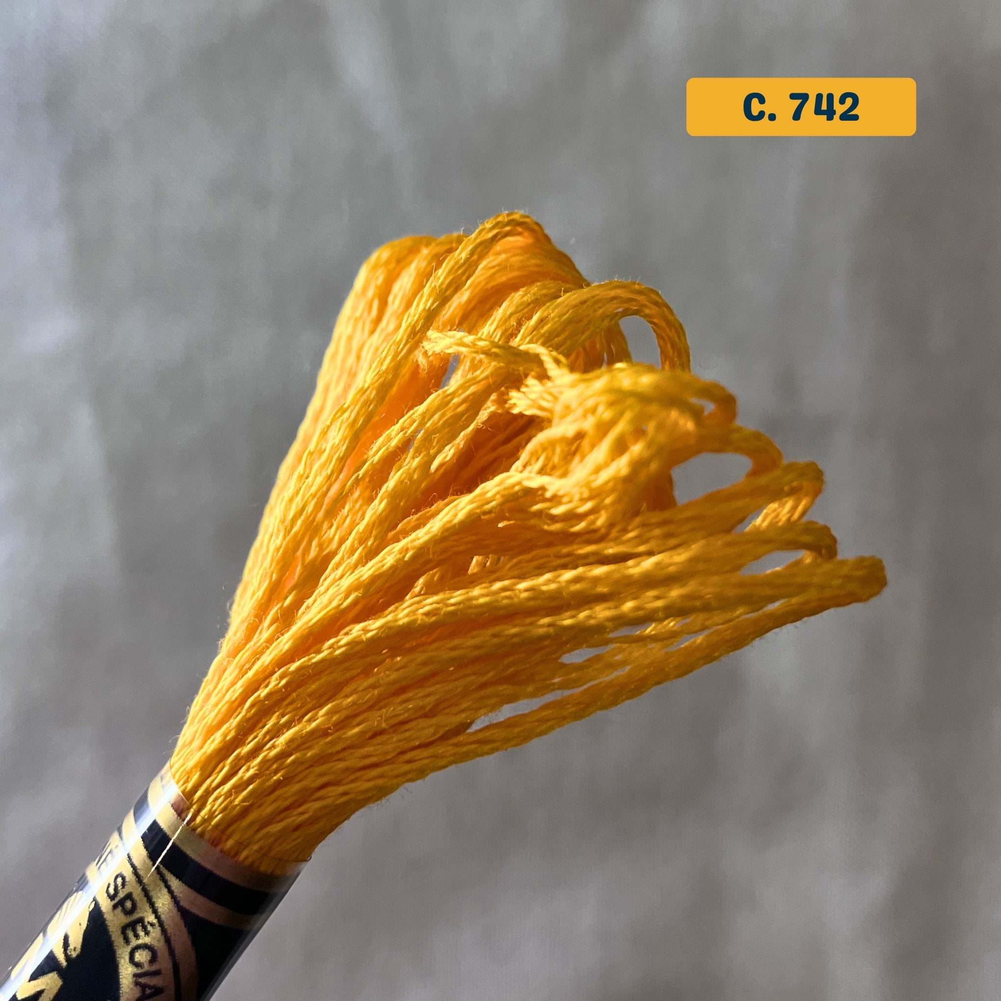 DMC 6-Strand Cotton Embroidery Floss – 742 Bright Orange-Yellow – 8m skein, 100% Egyptian cotton. Fabric background (blurred).