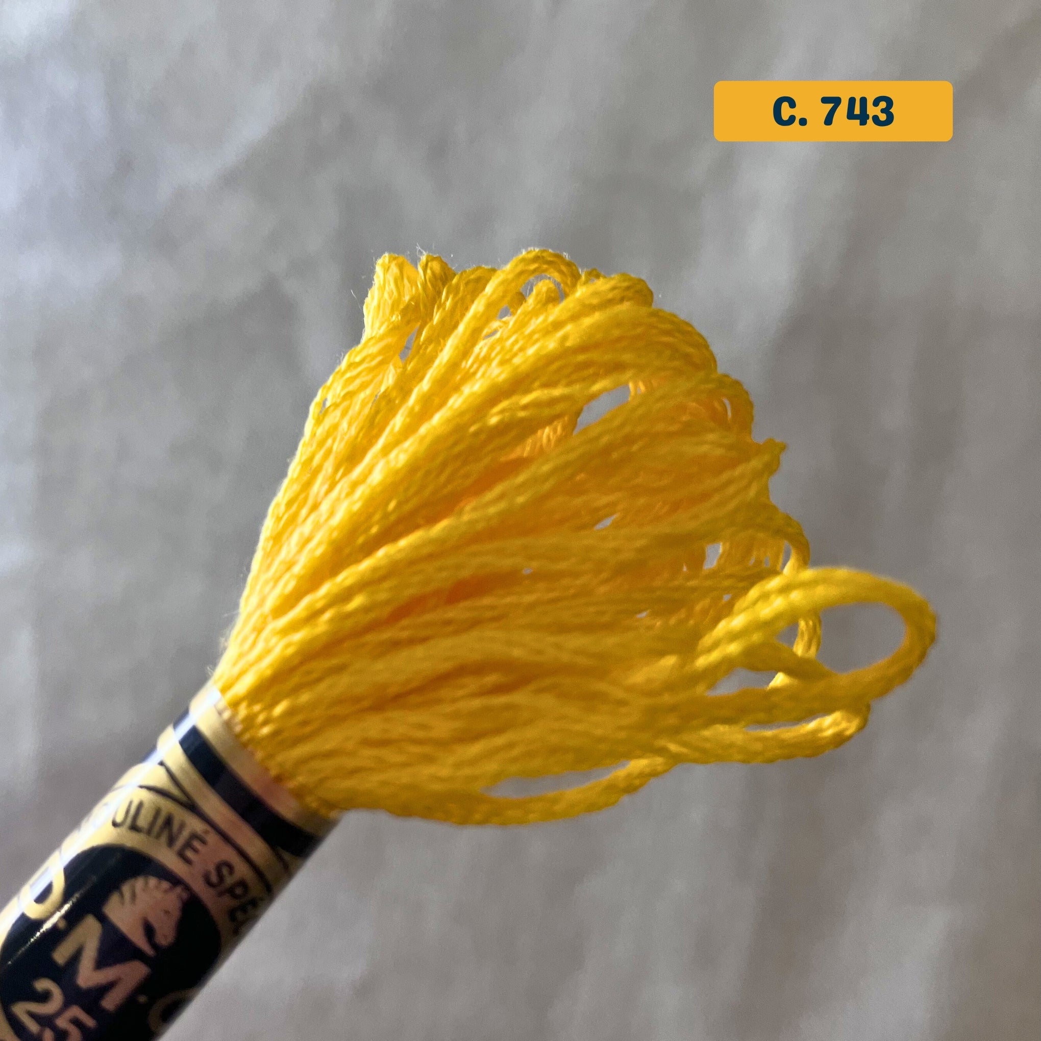 DMC 6-Strand Cotton Embroidery Floss – 743 Bright Yellow – 8m skein, 100% Egyptian cotton. Fabric background (blurred).