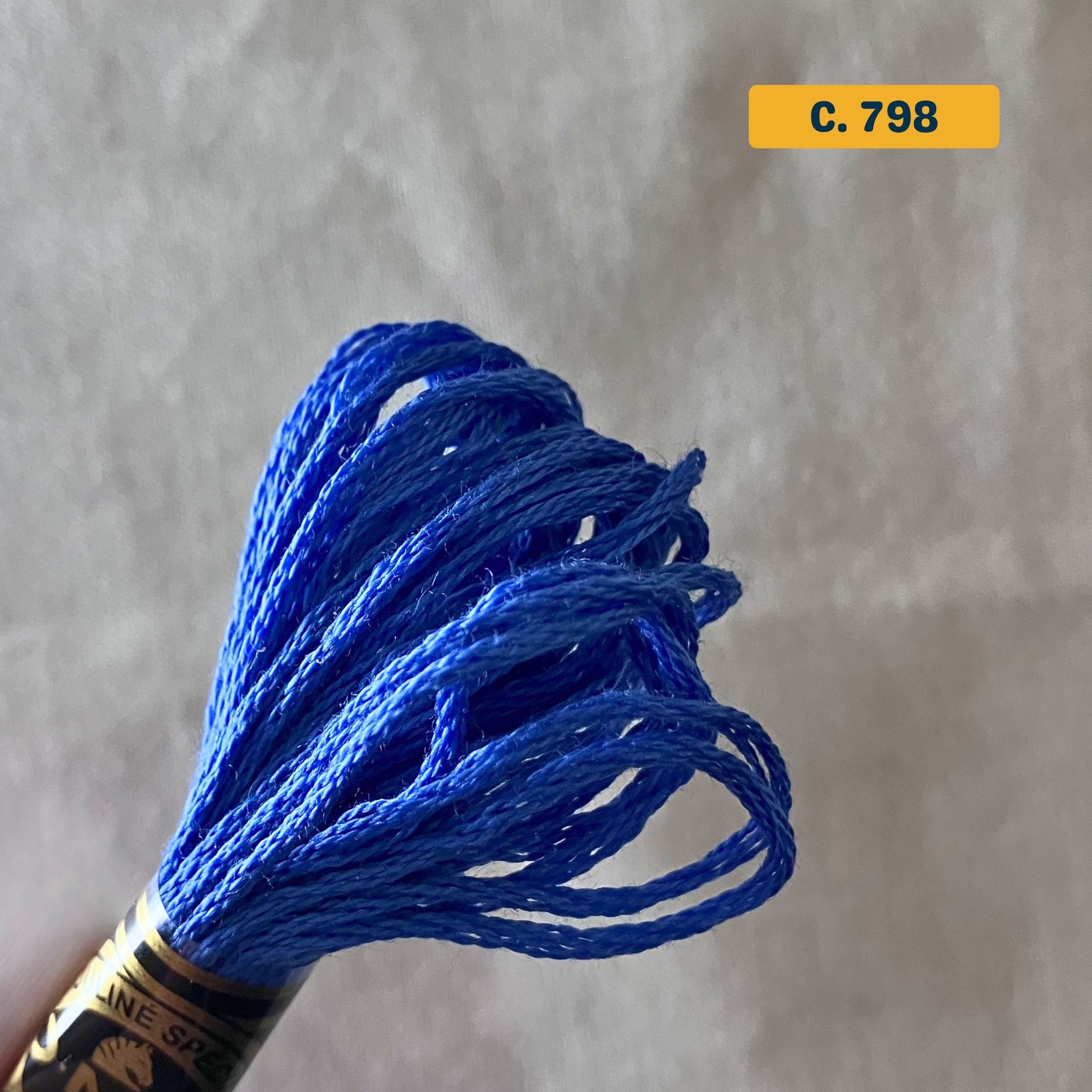 DMC 6-Strand Cotton Embroidery Floss – 798 Royal Blue – 8m skein, 100% Egyptian cotton. Fabric background (blurred).