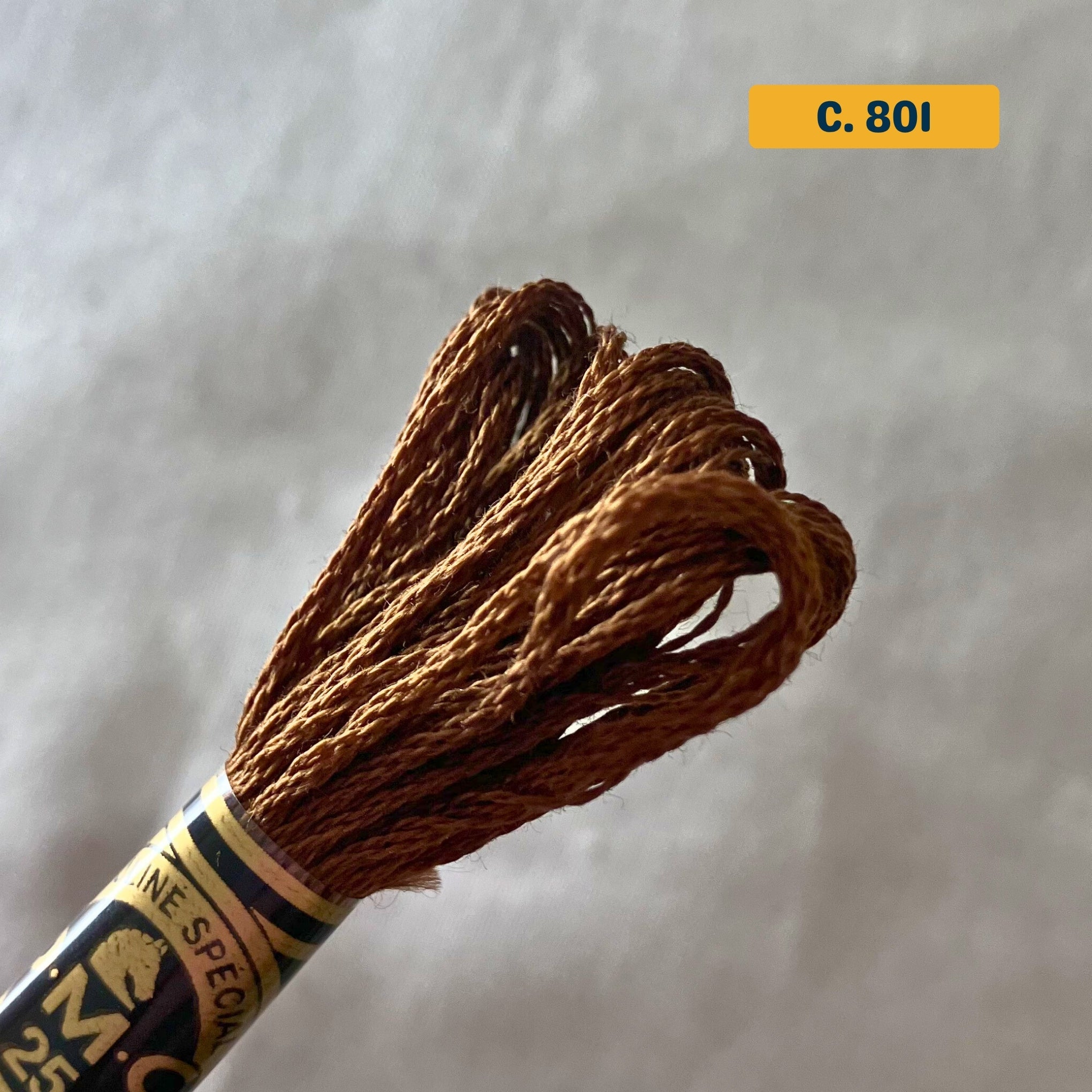 DMC 6-Strand Cotton Embroidery Floss – 801 Medium Brown – 8m skein, 100% Egyptian cotton. Fabric background (blurred).