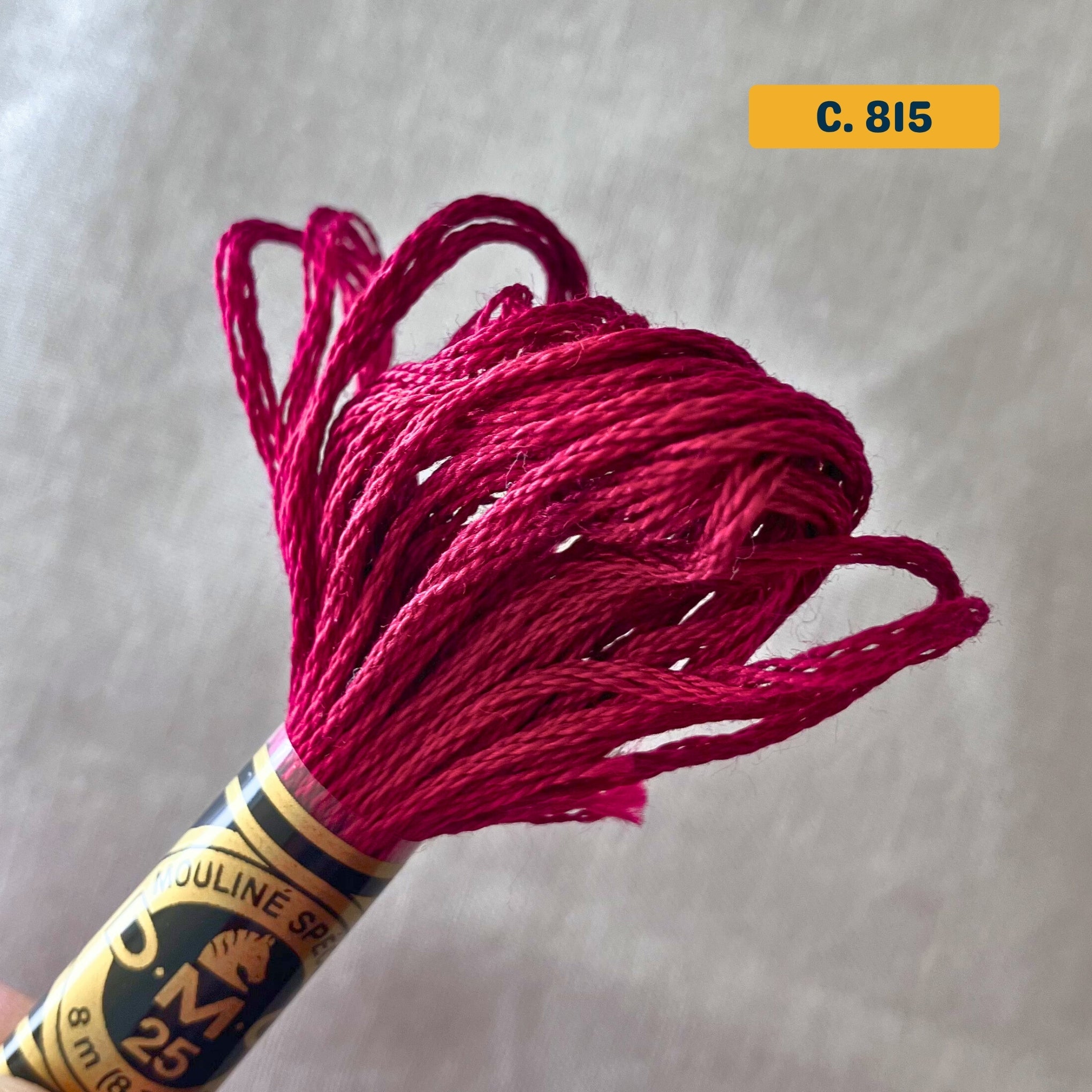 DMC 6-Strand Cotton Embroidery Floss – 815 Dark Red – 8m skein, 100% Egyptian cotton. Fabric background (blurred).