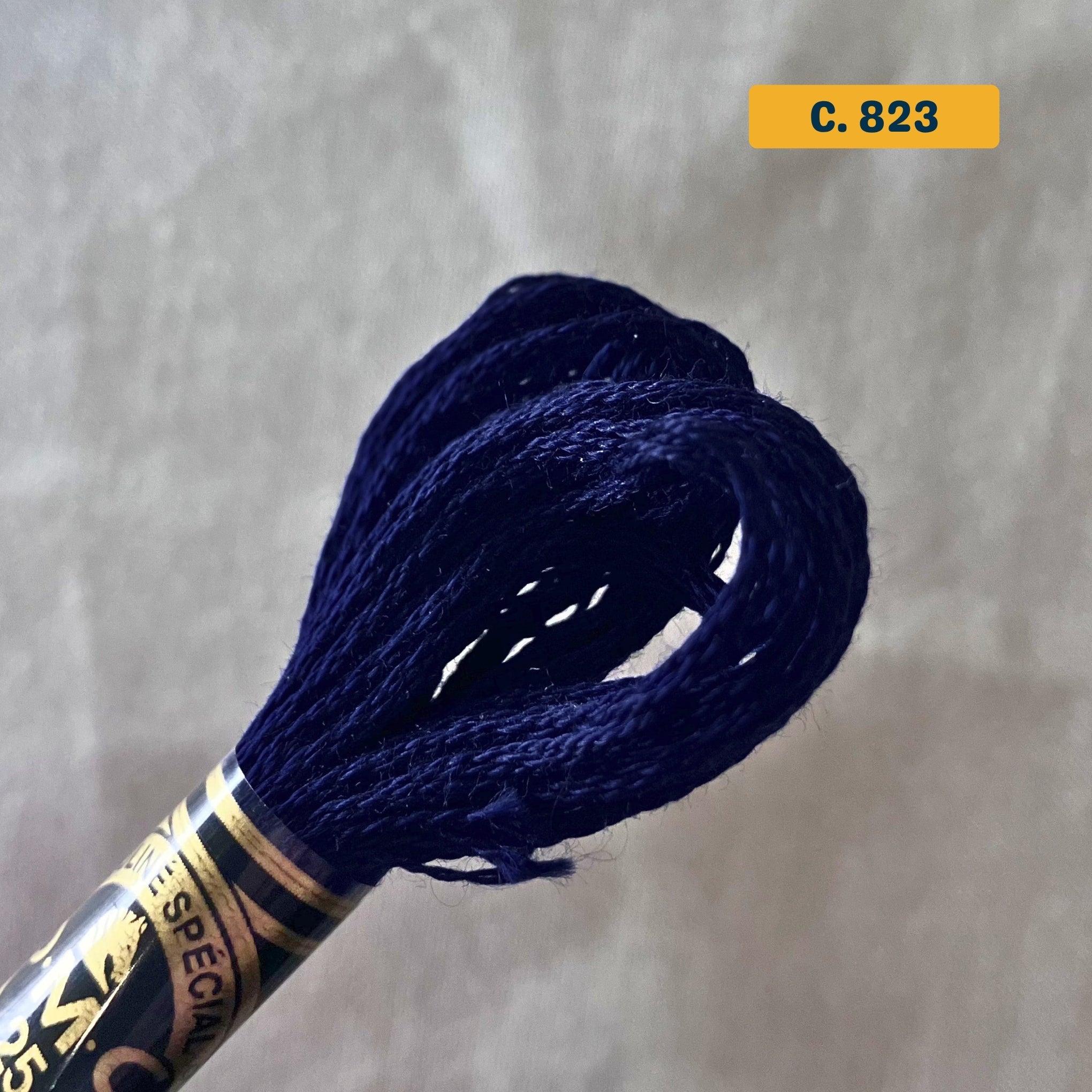 DMC 6-Strand Cotton Embroidery Floss – 823 Navy Blue – 8m skein, 100% Egyptian cotton. Fabric background (blurred).
