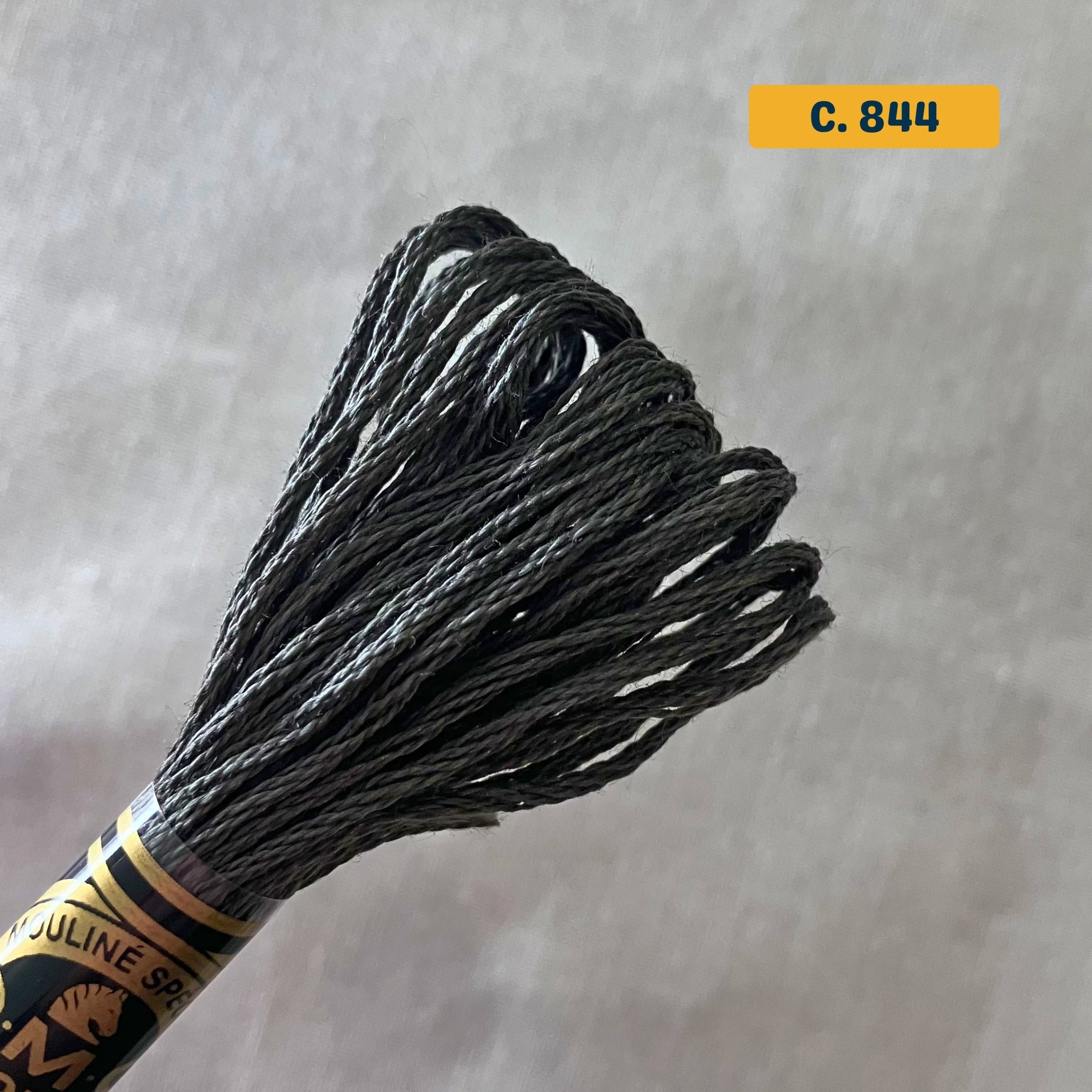 DMC 6-Strand Cotton Embroidery Floss – 844 Medium Grey – 8m skein, 100% Egyptian cotton. Fabric background (blurred).