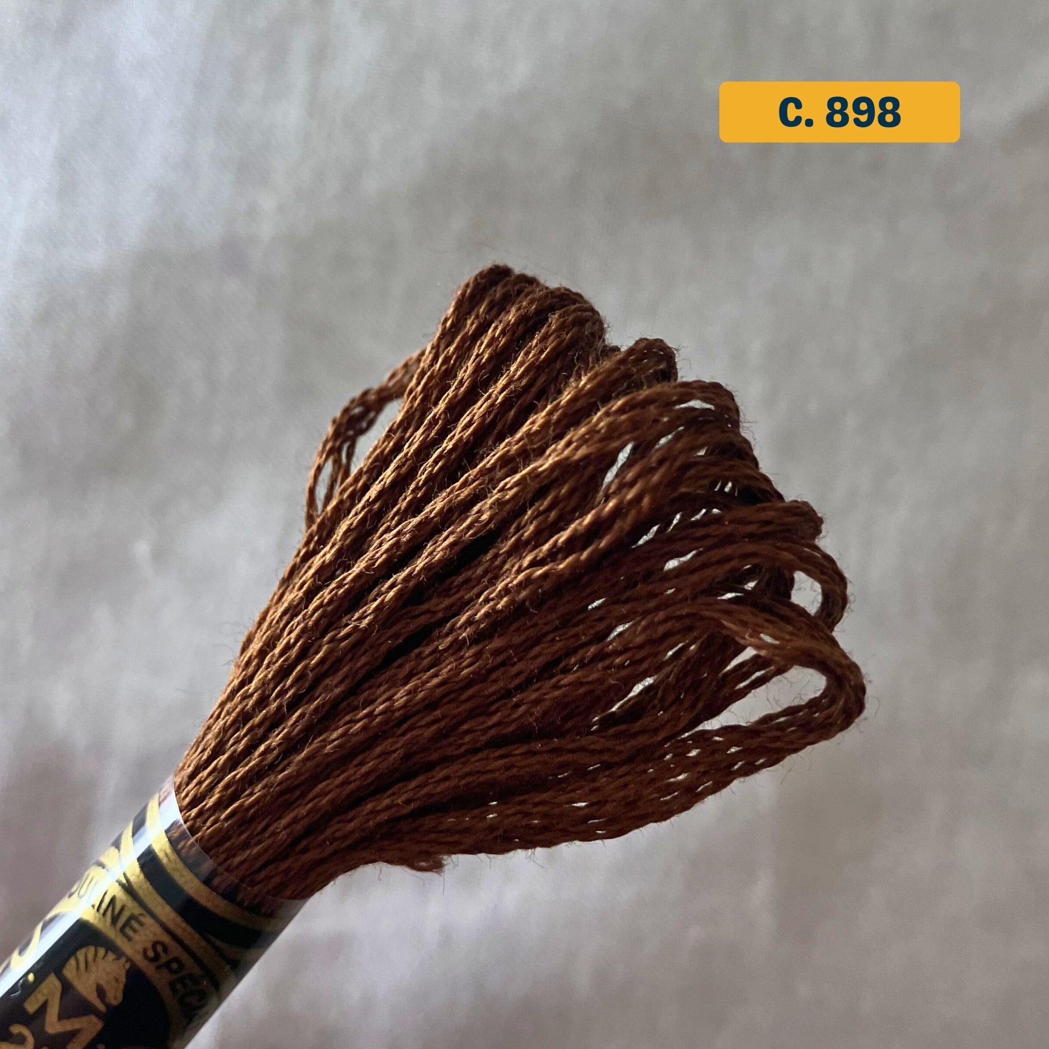 DMC 6-Strand Cotton Embroidery Floss – 898 Medium Brown – 8m skein, 100% Egyptian cotton. Fabric background (blurred).