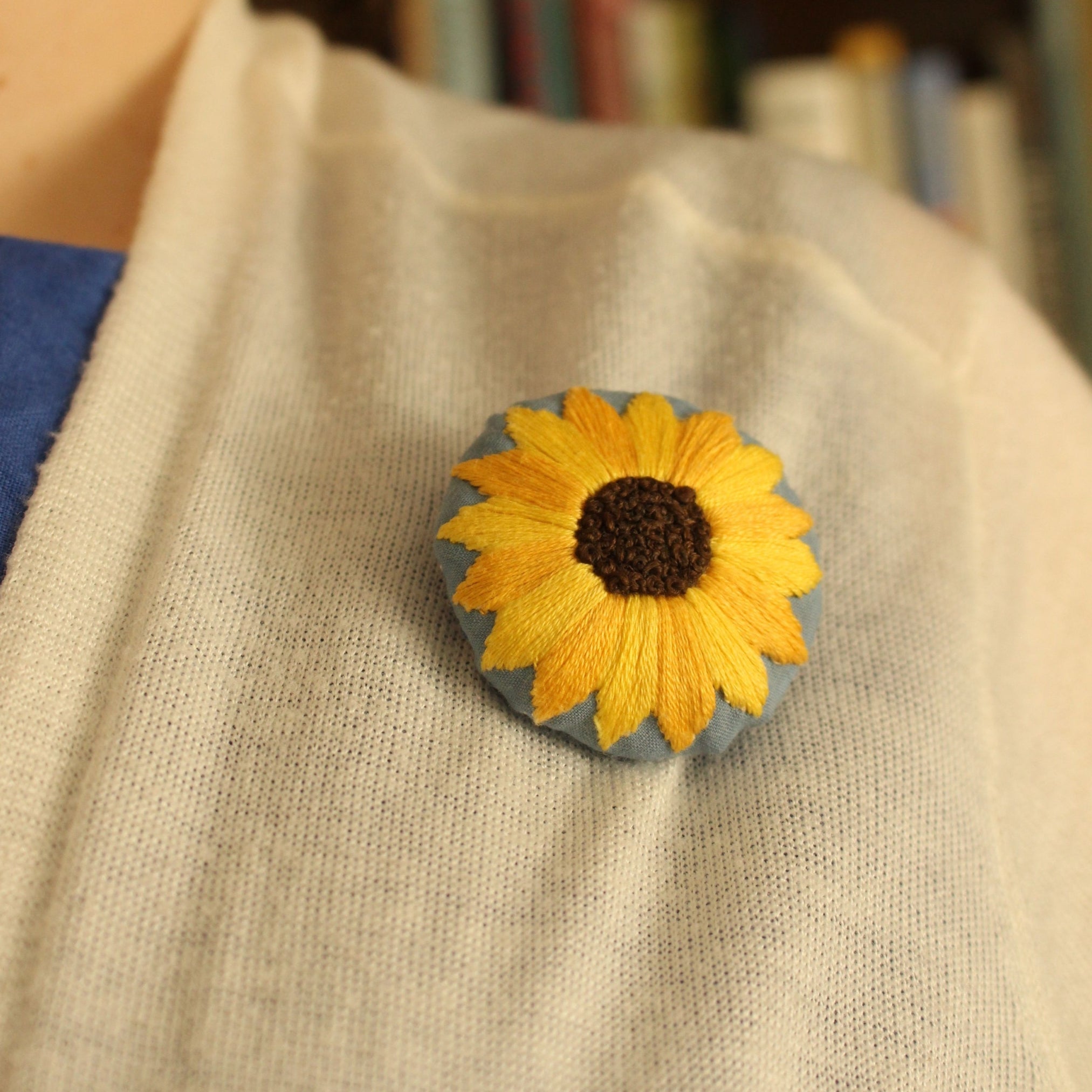 Finished embroidered brooch for Kelsey's beginner embroidery workshop at Stitch & Knit Dartmouth. A close-up of a sunflower brooch, featuring bright yellow embroidered satin-stitch petals and a dark brown center of french knots.
